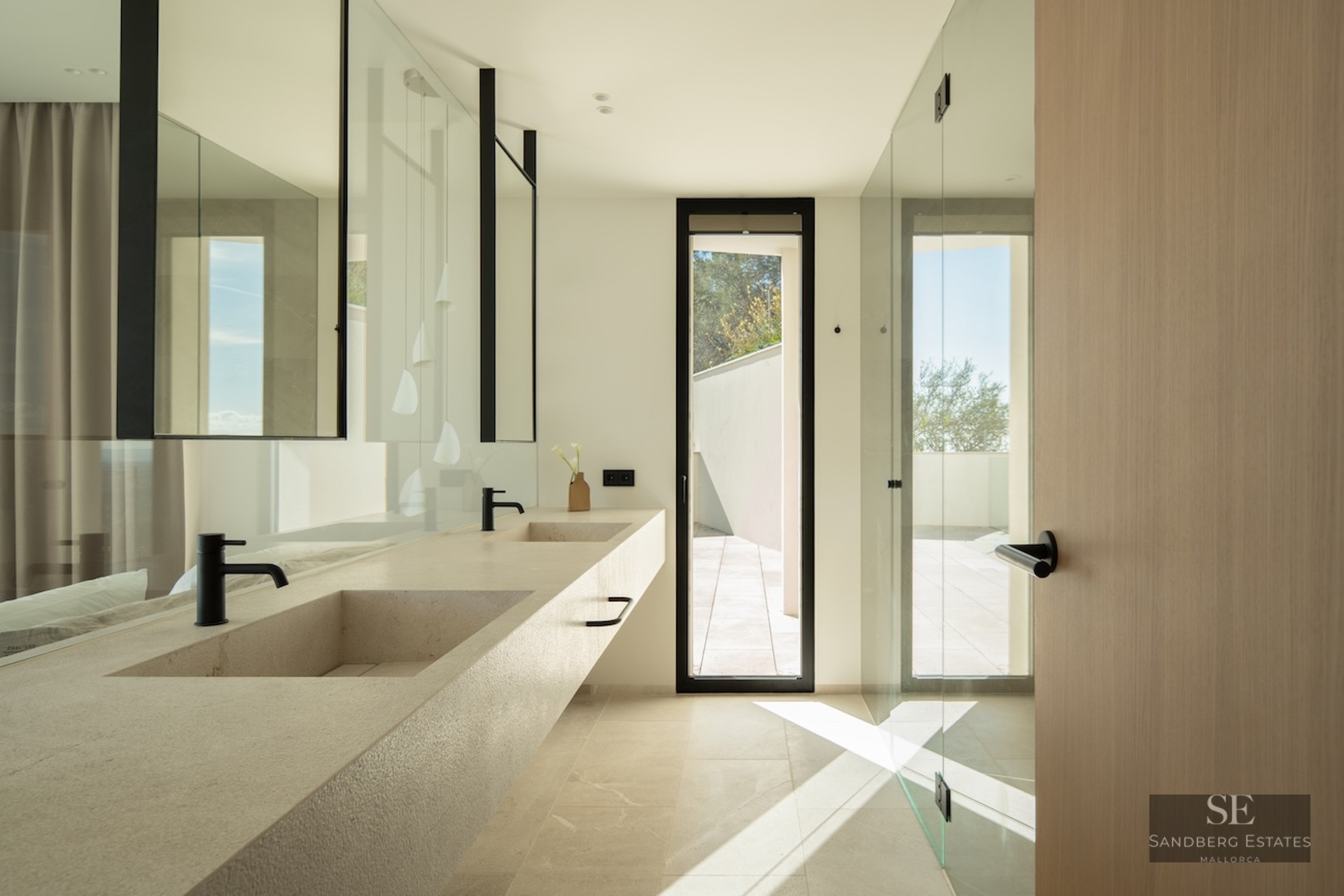 Modern bathroom featuring a long stone double vanity with black faucets, large mirrors, and natural light from a window.