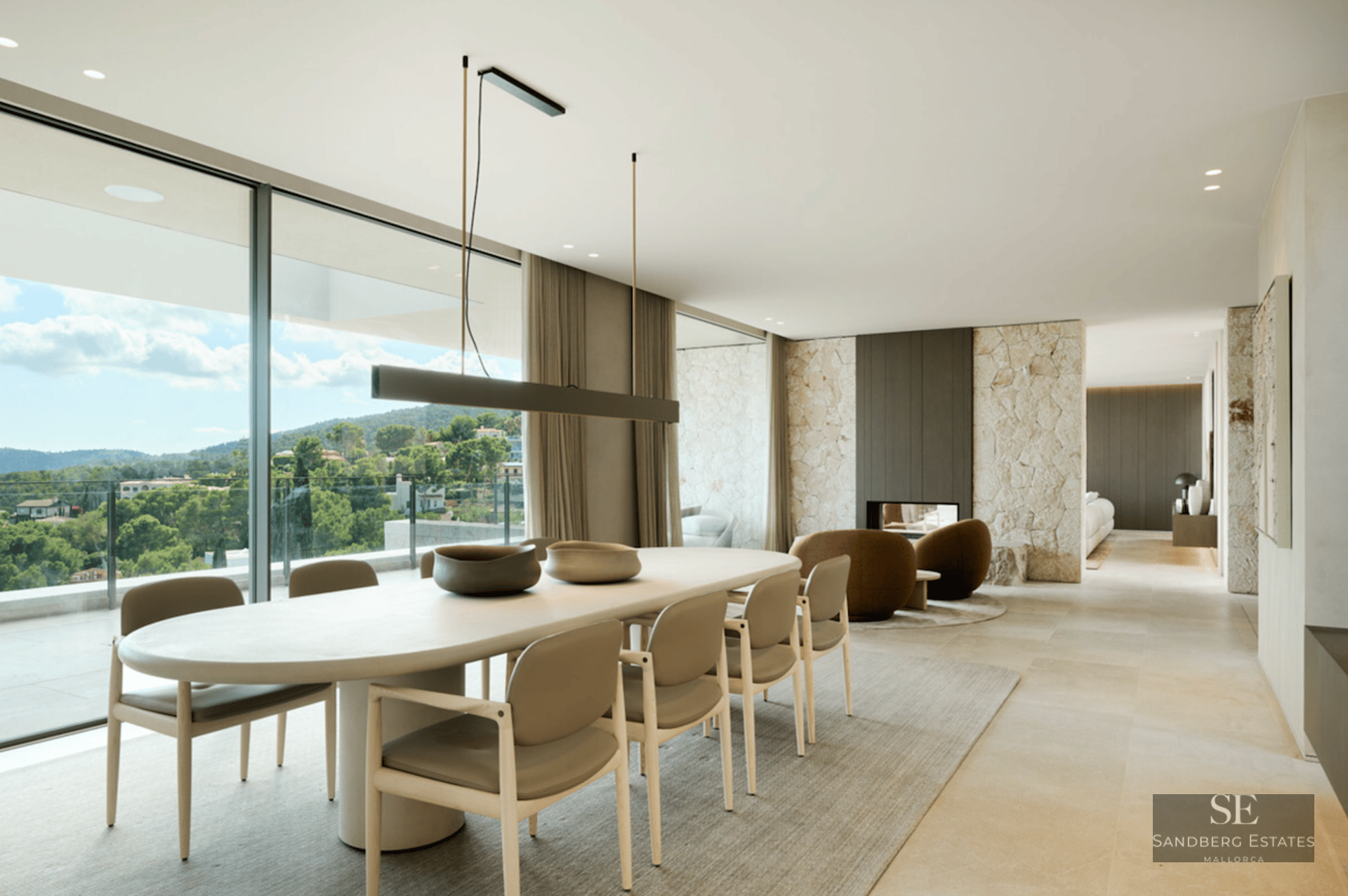 Modern dining area featuring an oval table, stone feature walls, and floor-to-ceiling windows overlooking a lush landscape.