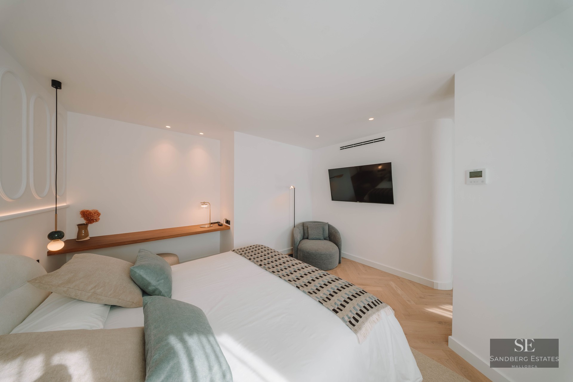 Modern bedroom featuring a white bed with sage green pillows, wooden shelf, and herringbone wood flooring.
