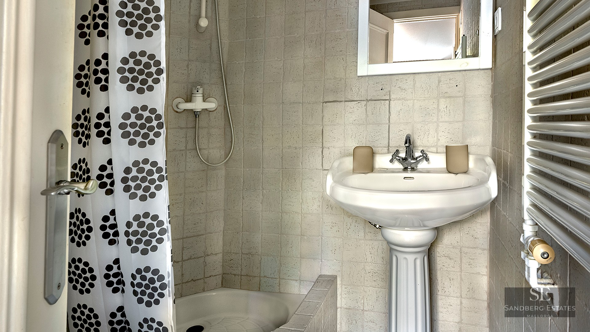 Small bathroom featuring a white pedestal sink, tiled walls, and a shower with a patterned polka-dot curtain.