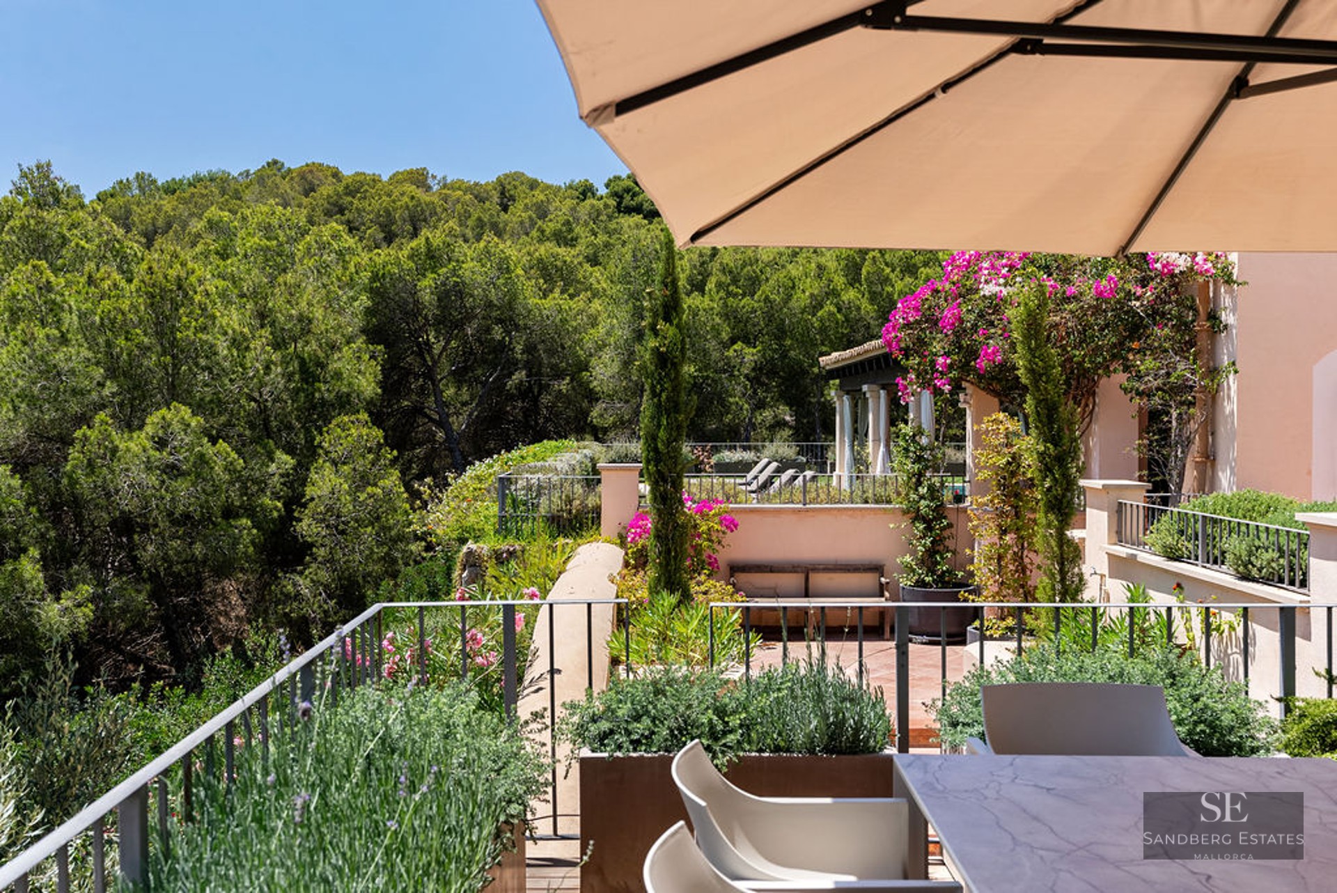 Terrace with a marble dining table and sun umbrella overlooking a lush green pine forest under a clear blue sky.
