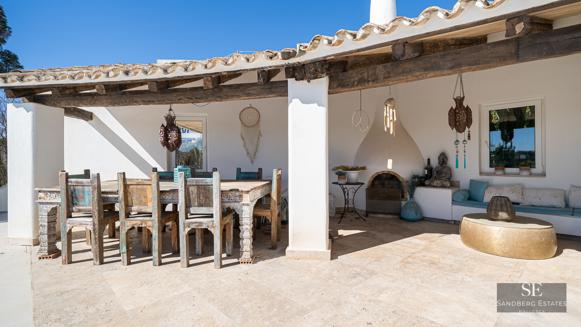 A covered terrace with a rustic wooden dining set, stone flooring, a built-in fireplace, and Mediterranean decor.