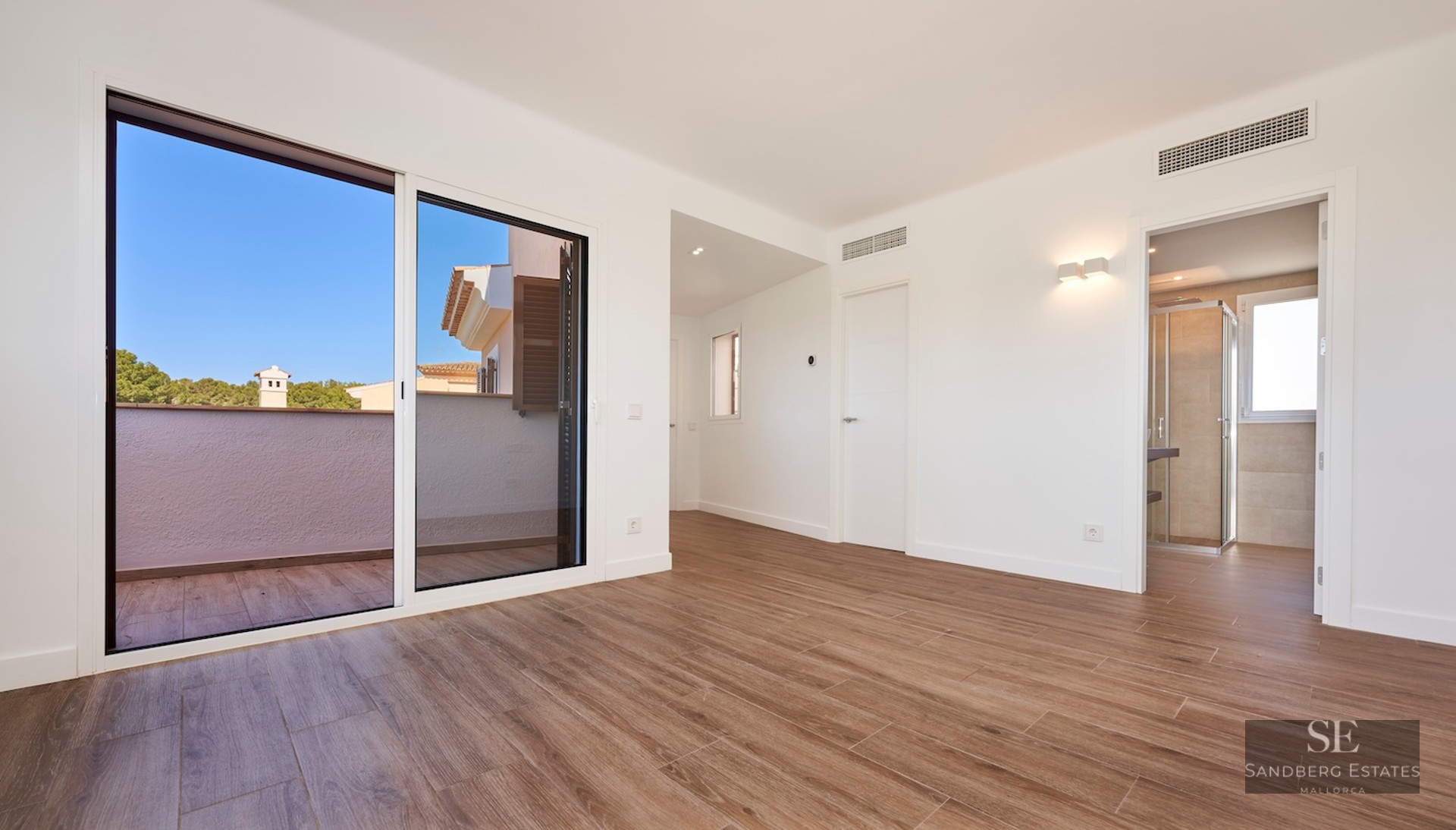 Bright empty room with wood-look floors, large sliding glass doors to a terrace, and an ensuite bathroom visible.