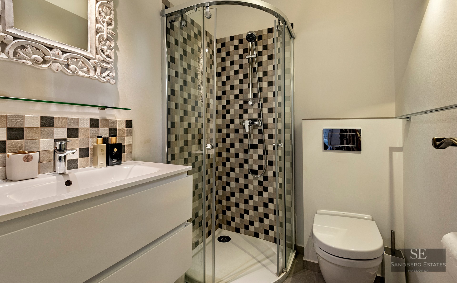 Modern bathroom featuring a curved glass corner shower with checkered tiles, a white vanity, and an ornate mirror.