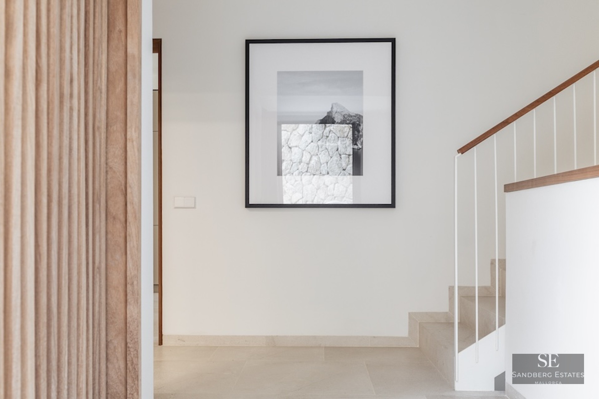 Minimalist hallway with stone stairs, a wooden handrail, and a large framed artwork on a white wall.