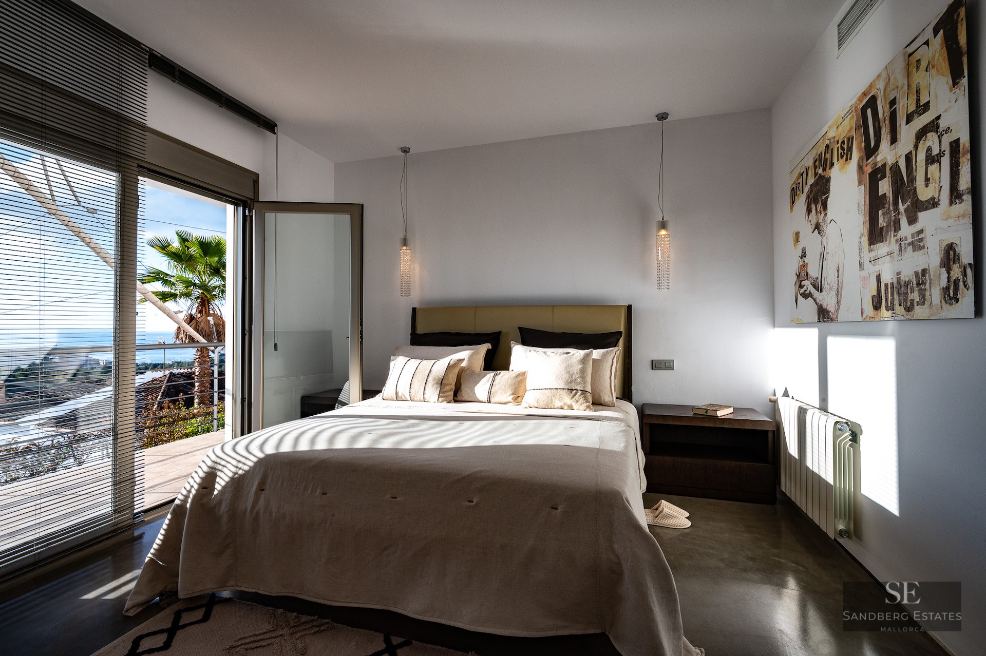 Bright bedroom featuring a large bed, polished concrete floors, and glass doors opening to a sunny private terrace.