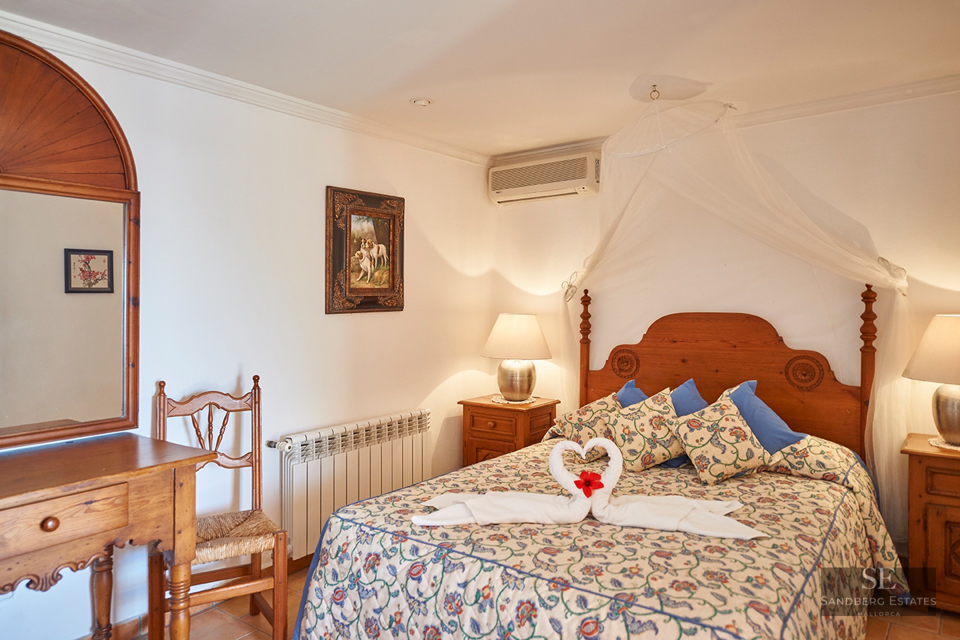 Cozy bedroom with a wooden bed, white mosquito net canopy, floral bedding, and rustic wooden furniture.