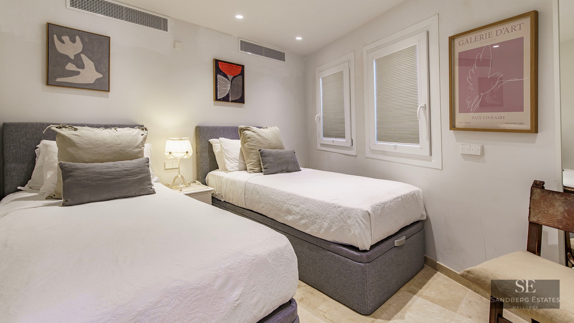 Bedroom with two single beds, grey headboards, white linens, and contemporary wall art.