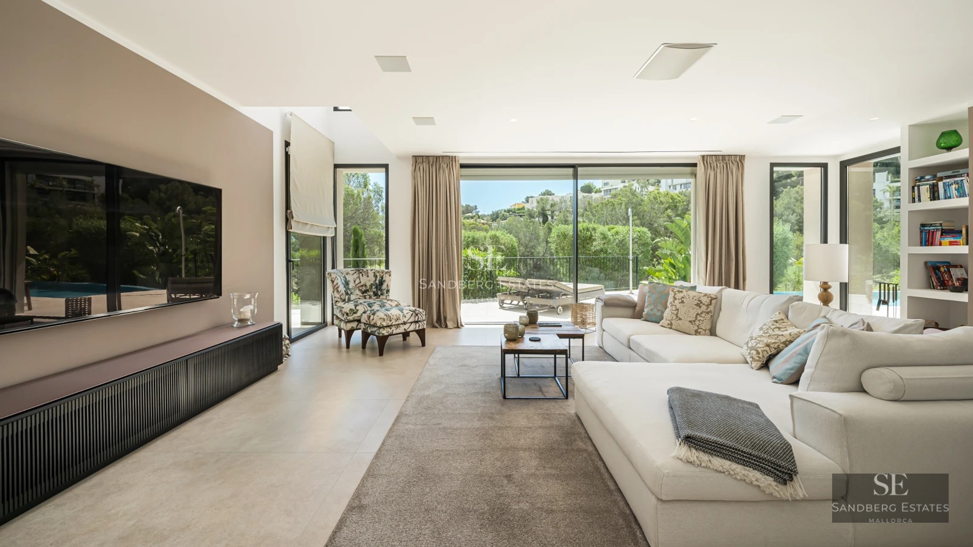 Spacious living room with floor-to-ceiling windows, light wood floors and minimalist design furniture. Views of pool and lush garden.