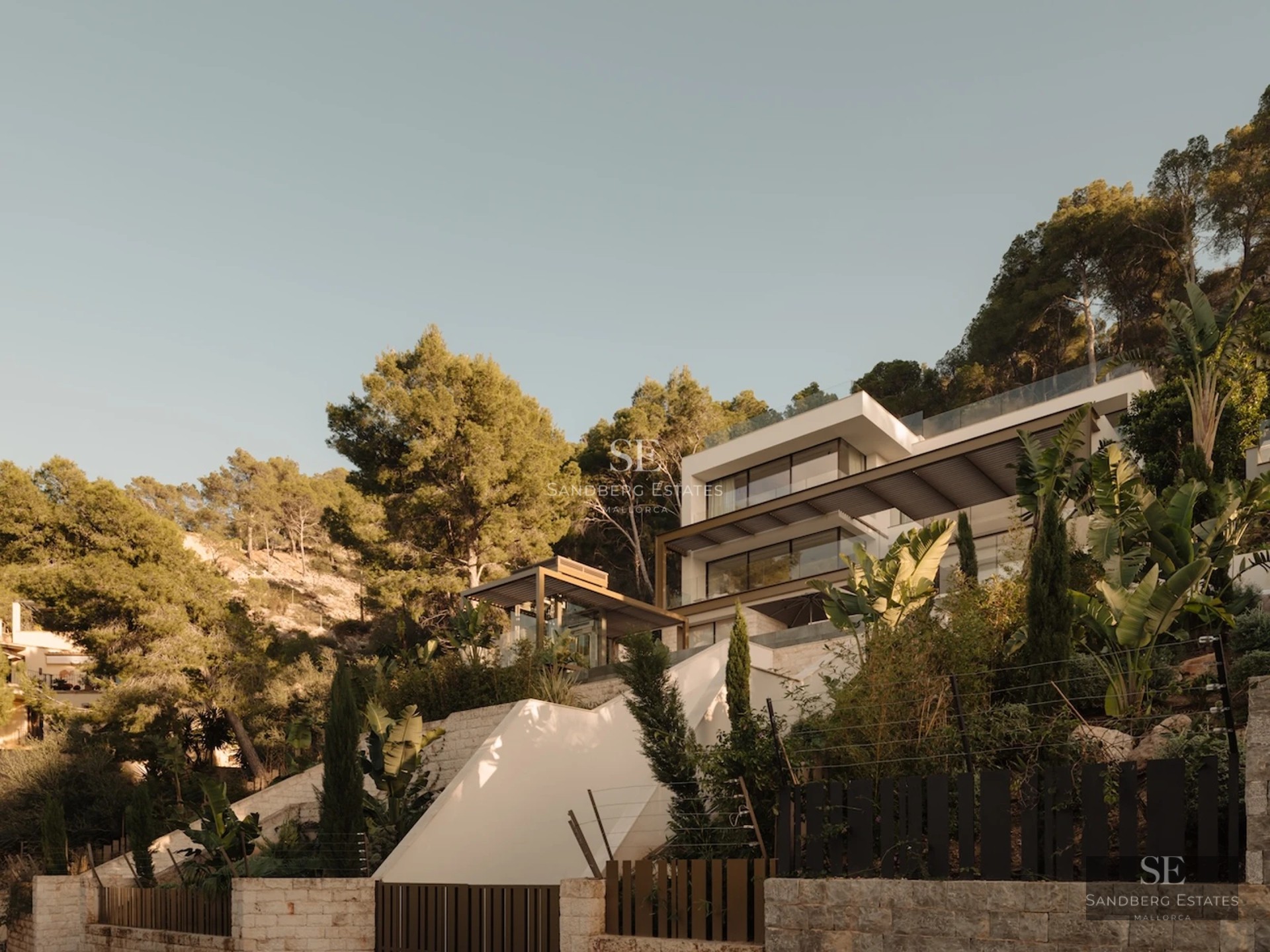 Exterior view of a luxurious house with infinity pool, manicured garden, and modern architecture. Large windows and natural light.