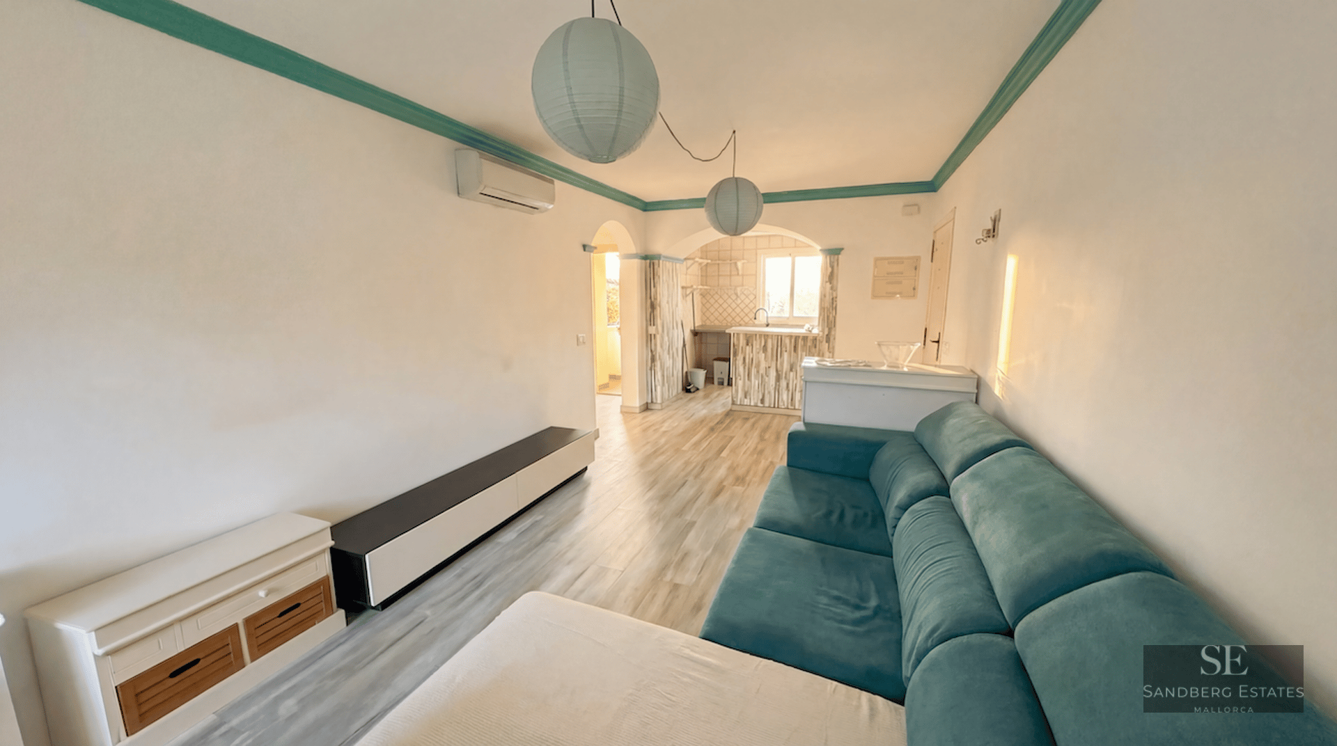 A living room featuring a turquoise sofa, wooden floors, and spherical paper lanterns next to an archway.