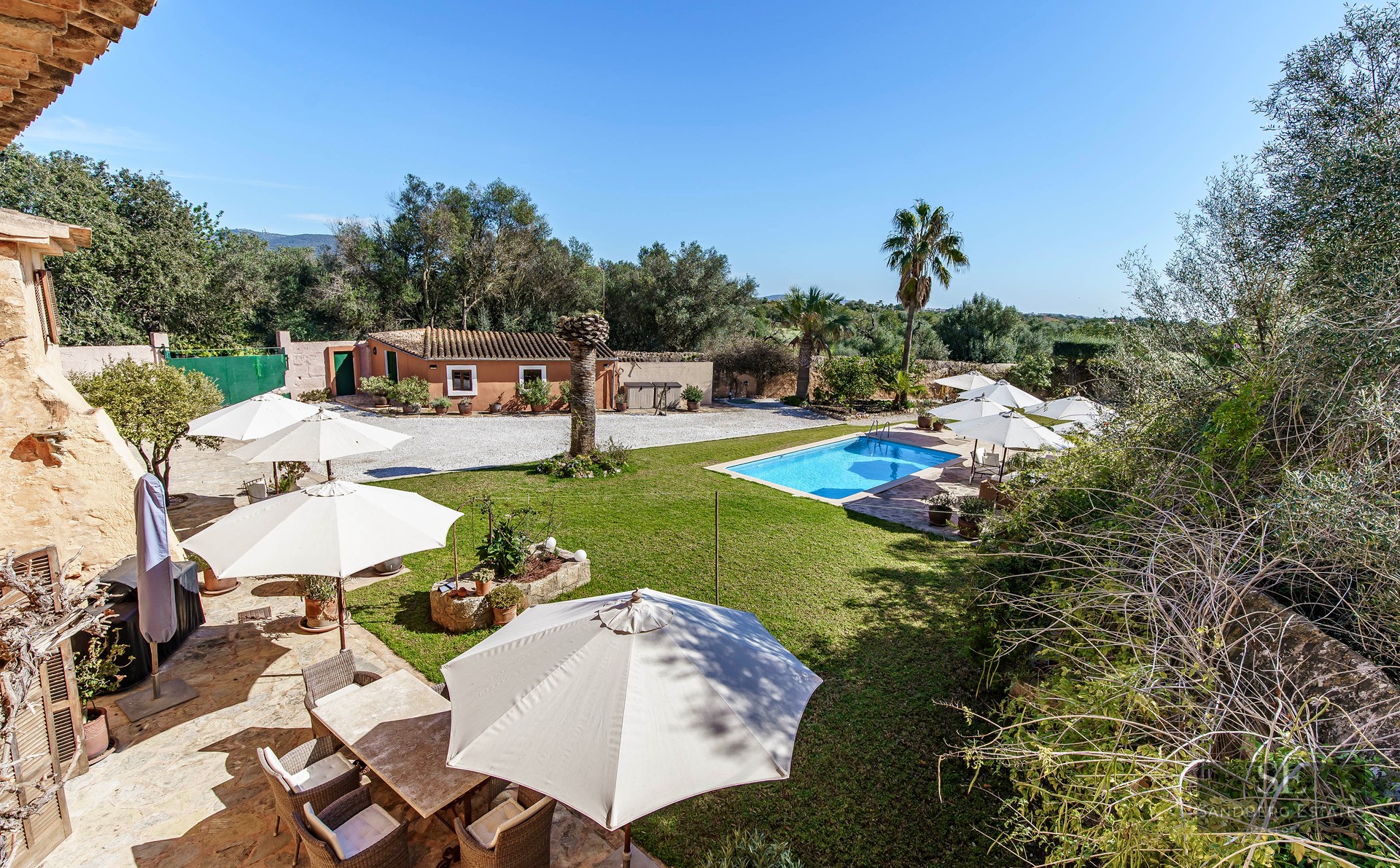 Rectangular swimming pool surrounded by green lawn, sun umbrellas, and a stone terrace at a Mediterranean estate.