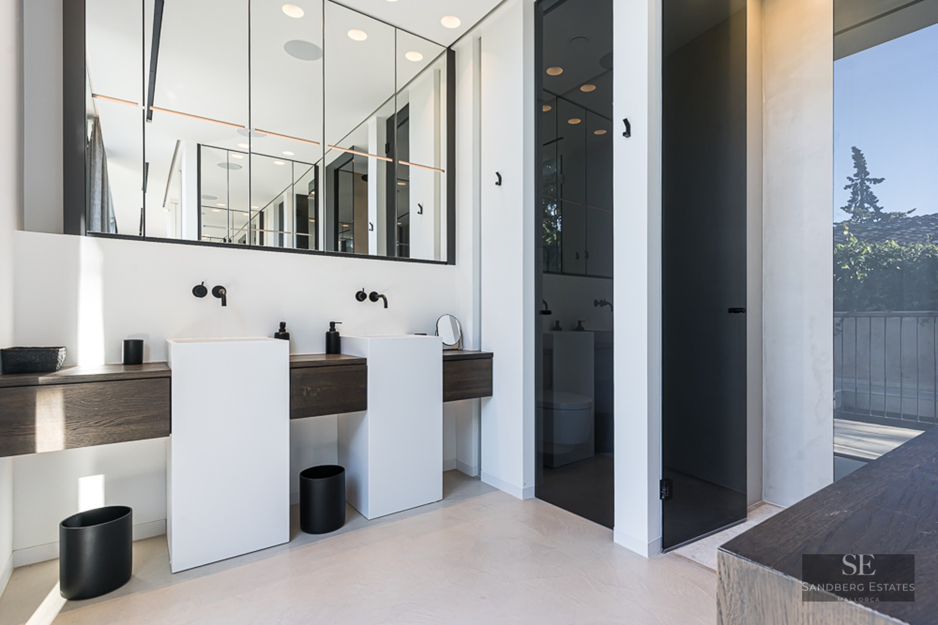 Modern bathroom featuring two white pedestal sinks, dark wood accents, and a large wall mirror.