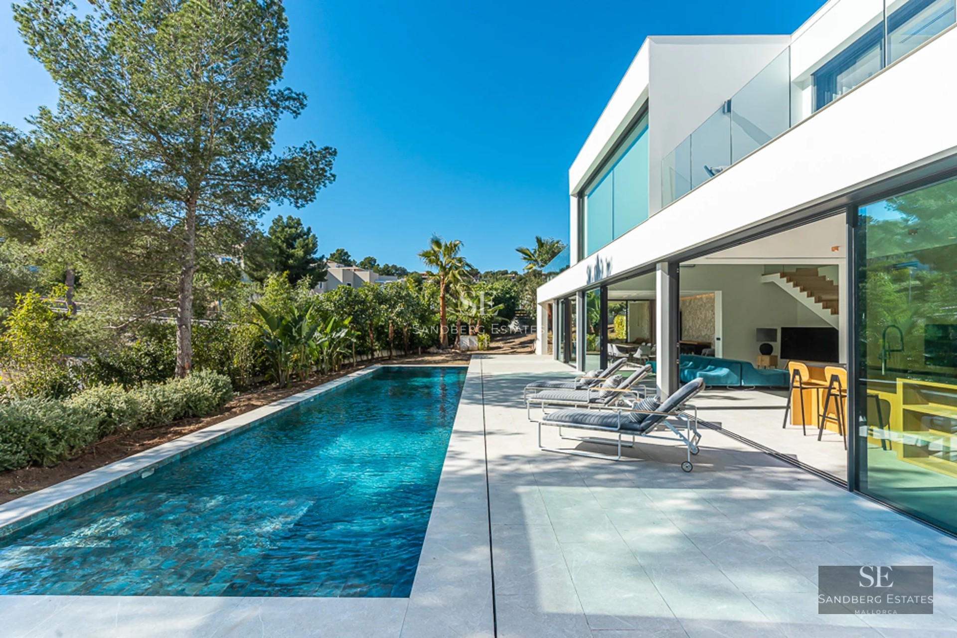 Vue d'une piscine moderne avec des chaises longues et des parasols. Architecture épurée et minimaliste, entourée de verdure.