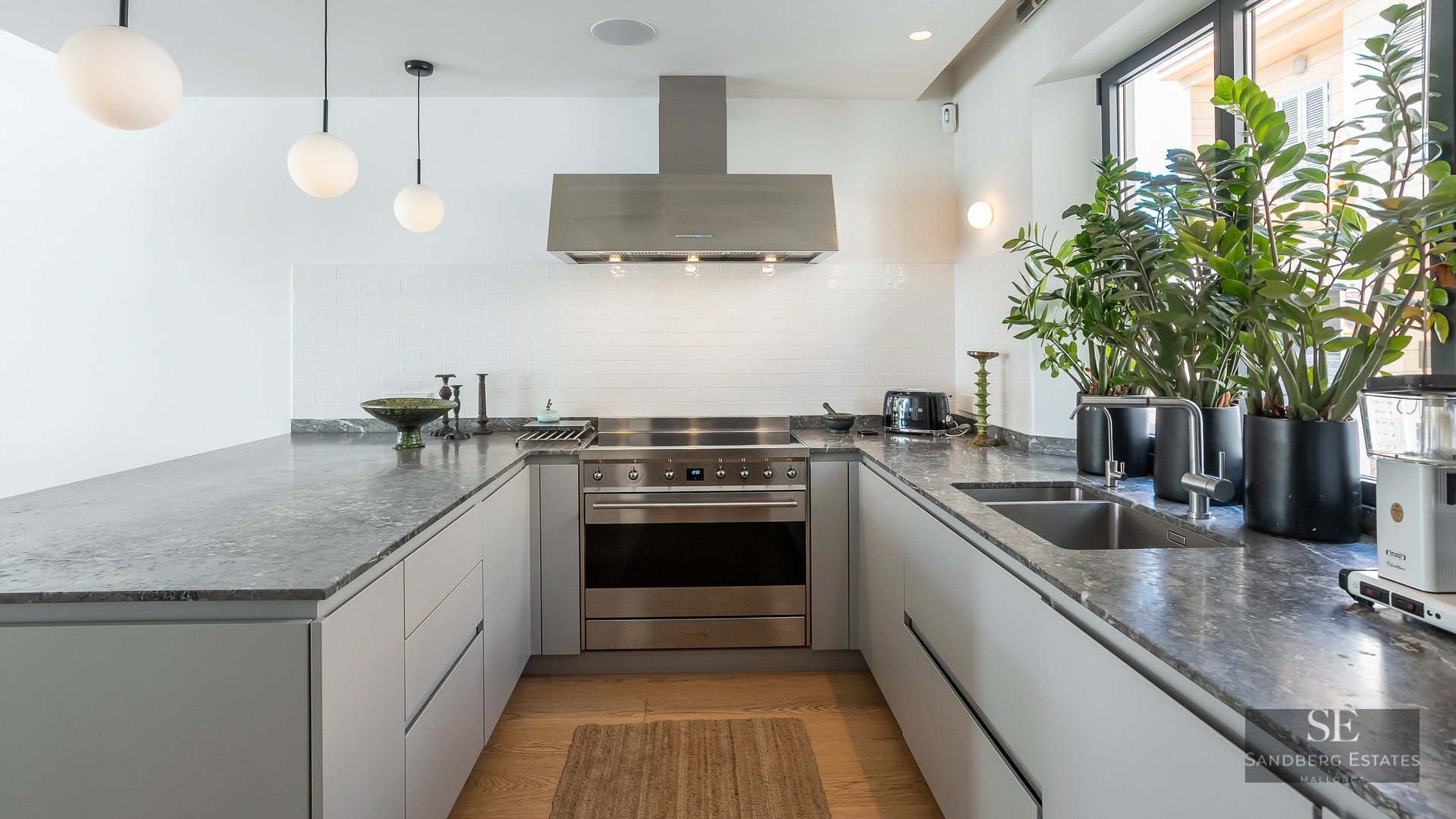 Modern U-shaped kitchen with grey stone countertops, stainless steel appliances, and natural light from a window.
