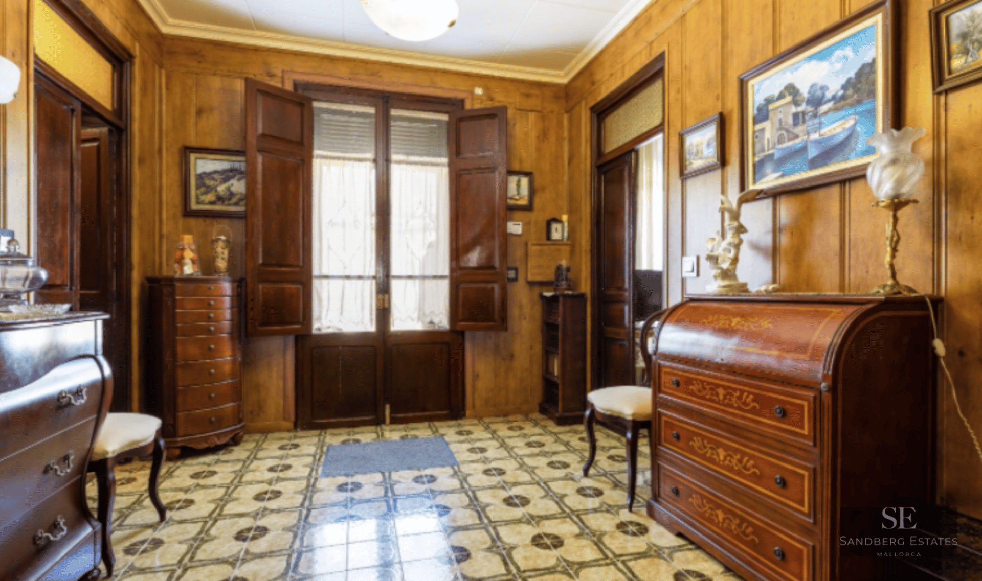 Entrance hall featuring warm wood-paneled walls, decorative patterned tile flooring, and classic antique furniture.