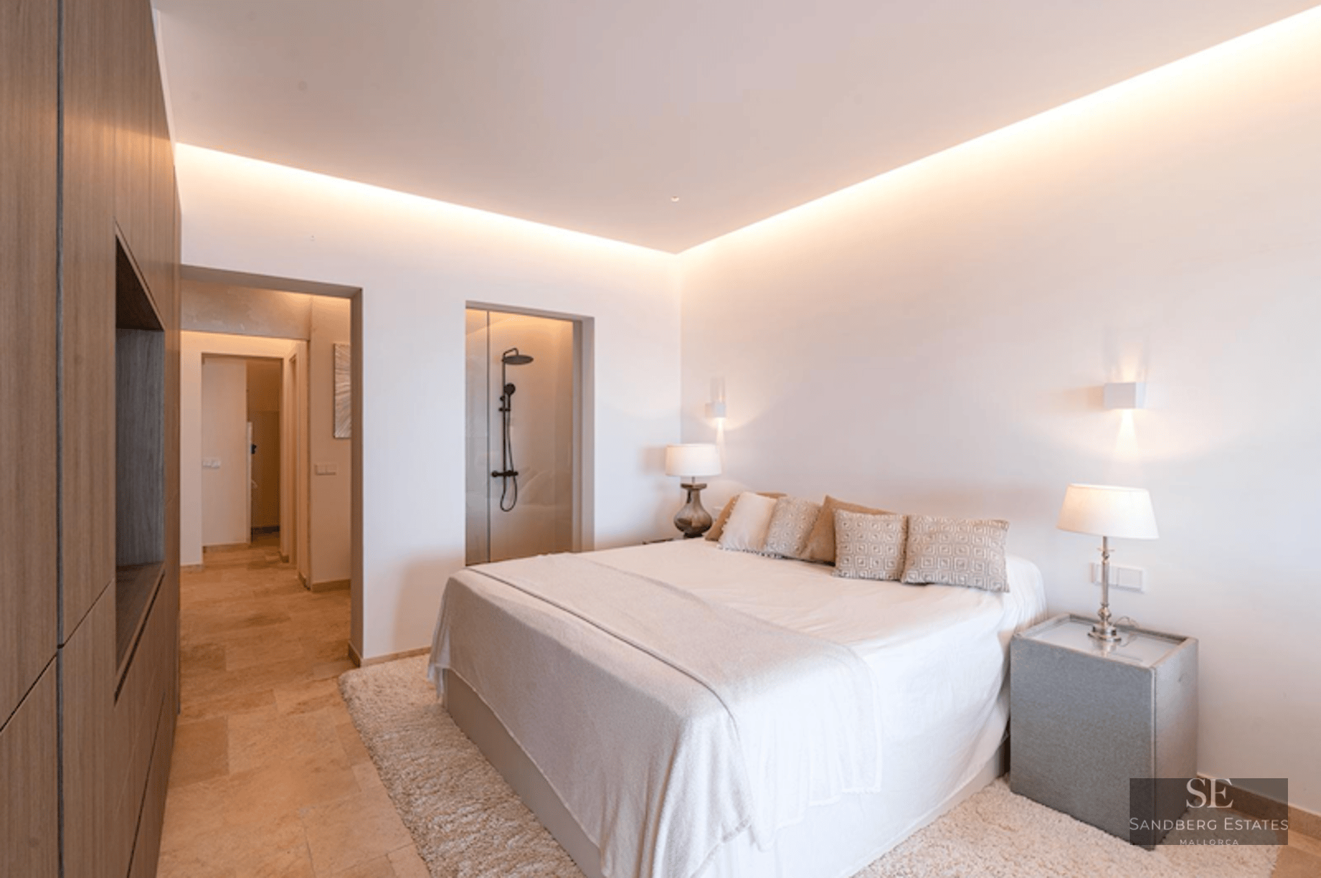 Luxury master bedroom featuring a large bed, warm cove lighting, wood wall panels, and a glass-enclosed shower.