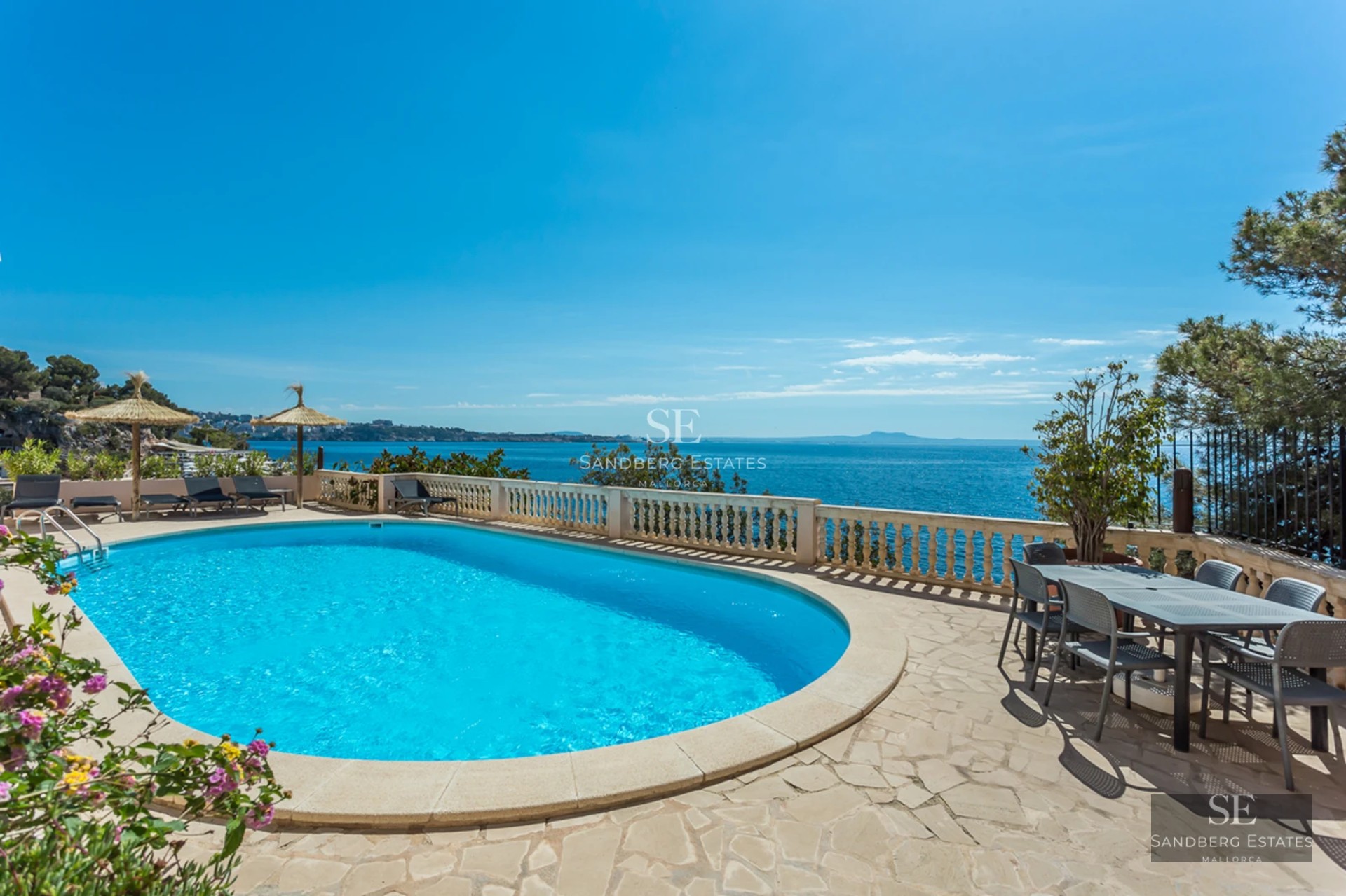 Oval swimming pool on a stone terrace overlooking the Mediterranean Sea under a clear blue sky.