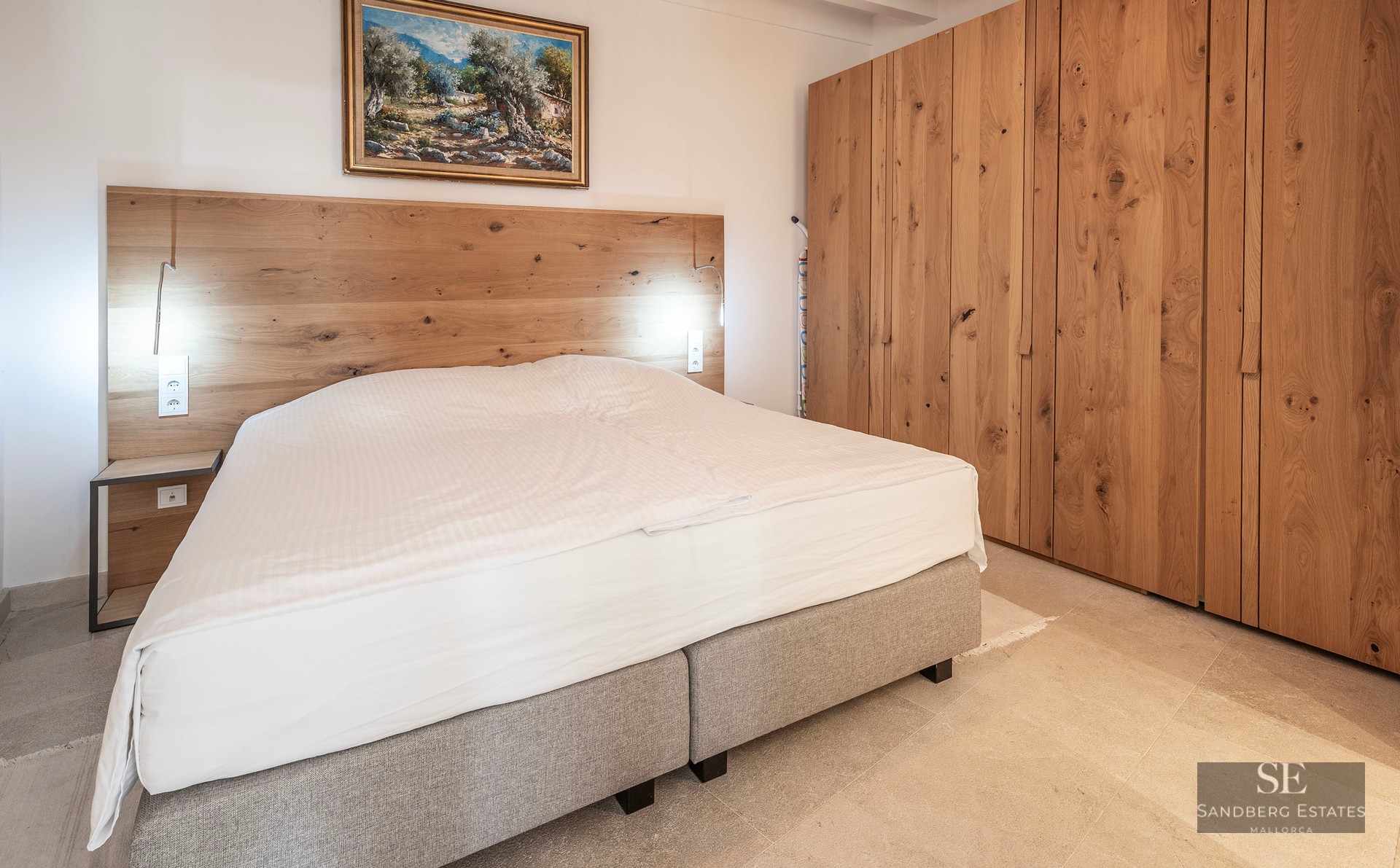 Chambre moderne avec un grand lit, une tête de lit en bois, de grandes armoires en chêne et un tableau au mur.