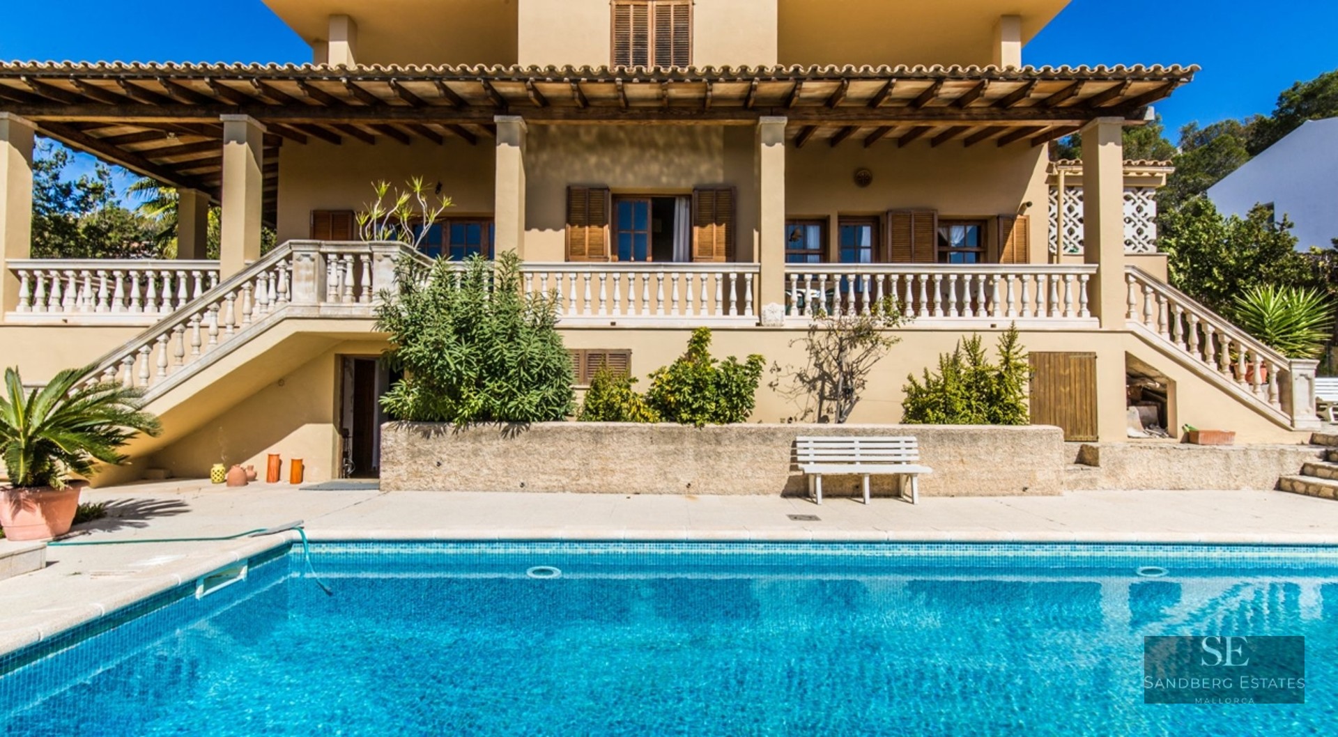 Mediterranean style villa with a large blue swimming pool and a stone balustrade terrace.