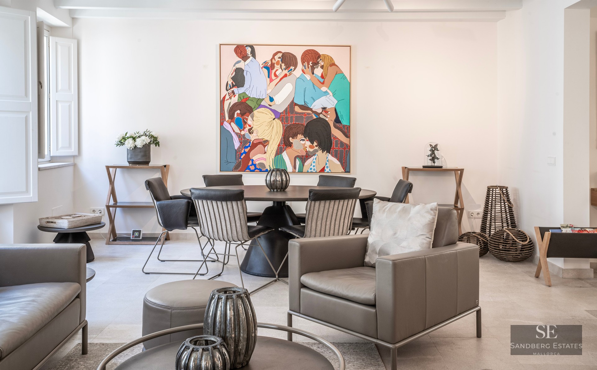 Pièce moderne lumineuse avec un fauteuil en cuir gris, une table à manger ronde et un grand tableau coloré au mur.
