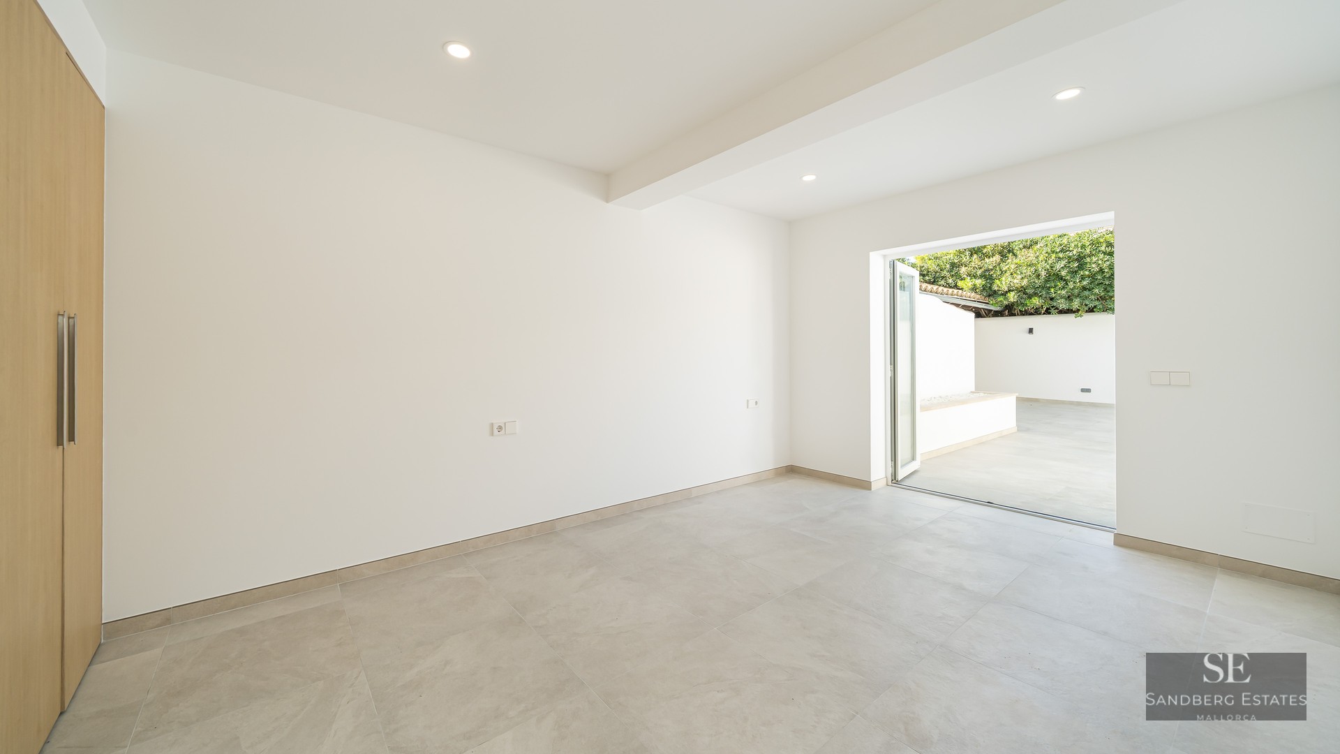 Bright, empty modern room with light gray tile floor, white walls, built-in wooden closet, and glass door to a patio.
