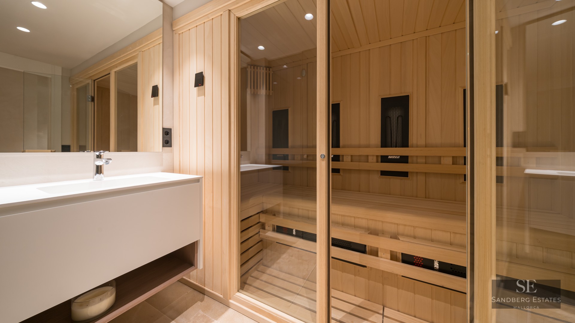Light wood sauna with glass doors next to a sleek white bathroom vanity and mirror.