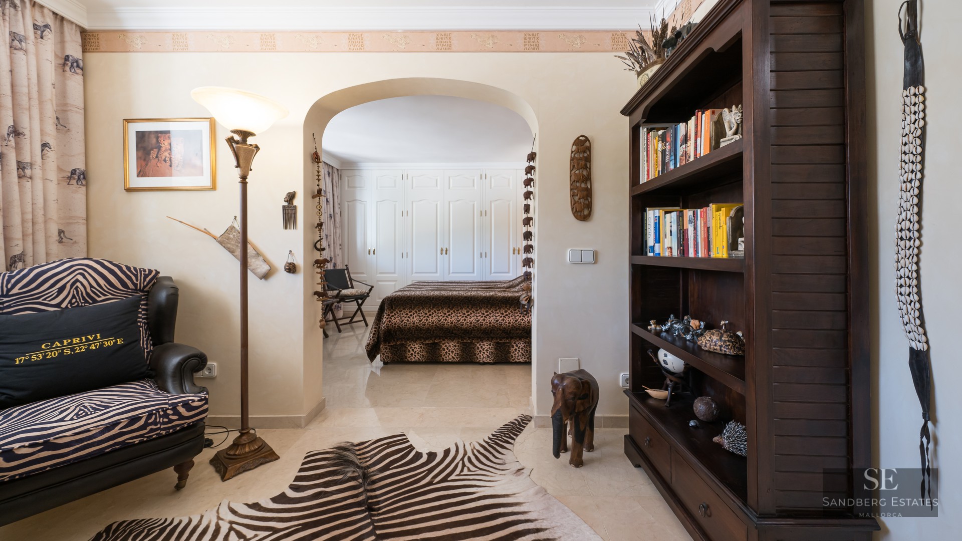 African-themed sitting room with zebra rug and chair leading through an archway to a bedroom with leopard print bedding.