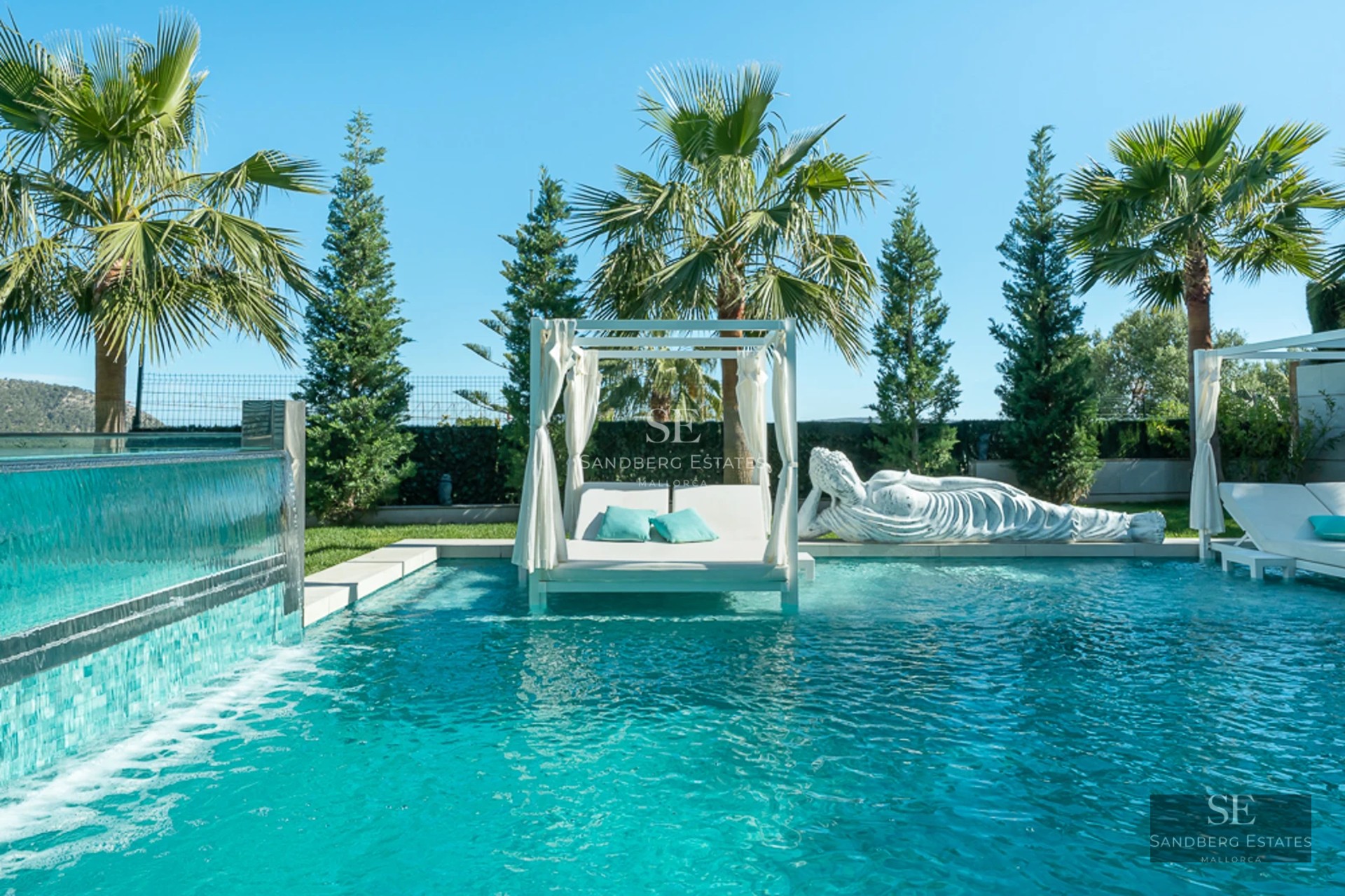 View of infinity pool with lounge chairs, surrounded by lush garden. Modern architecture with large windows and balcony.