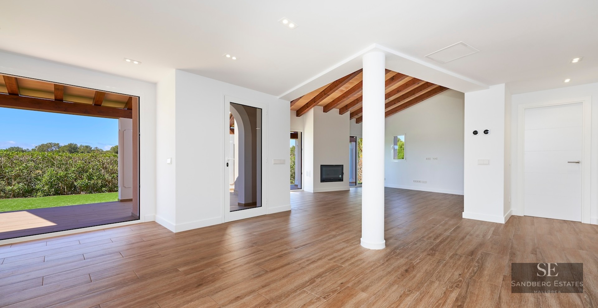 Open-plan living room with wood-look tile flooring, exposed beams, a white fireplace, and direct garden access.
