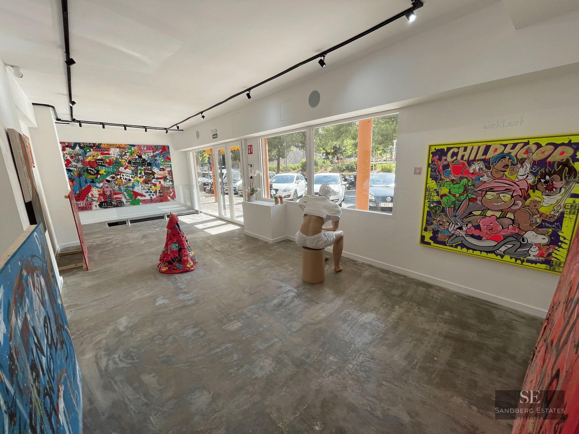 A modern art gallery with concrete floors, white walls, vibrant contemporary paintings, and a sitting sculpture.