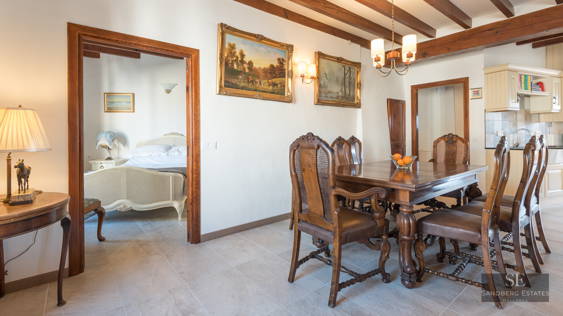 Dining room featuring a carved wood table, leather and cane chairs, beamed ceilings, and a view into a bedroom.