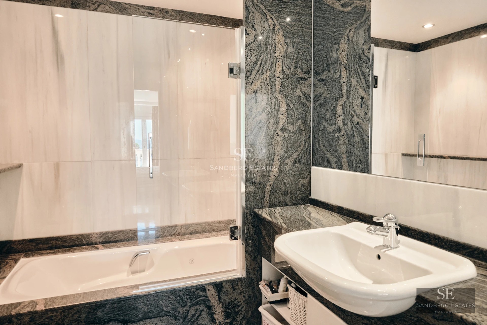 Bright, spacious living room with large windows and balcony overlooking the sea. Light wood floors and modern decor.