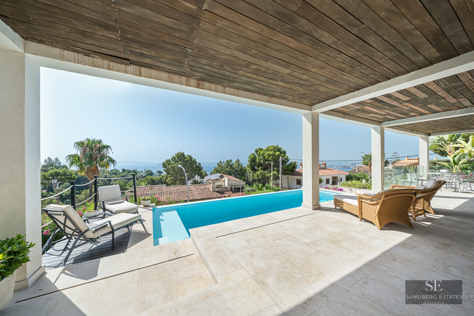 Covered terrace featuring a turquoise pool, sun loungers, and panoramic sea views under a rustic wooden ceiling.