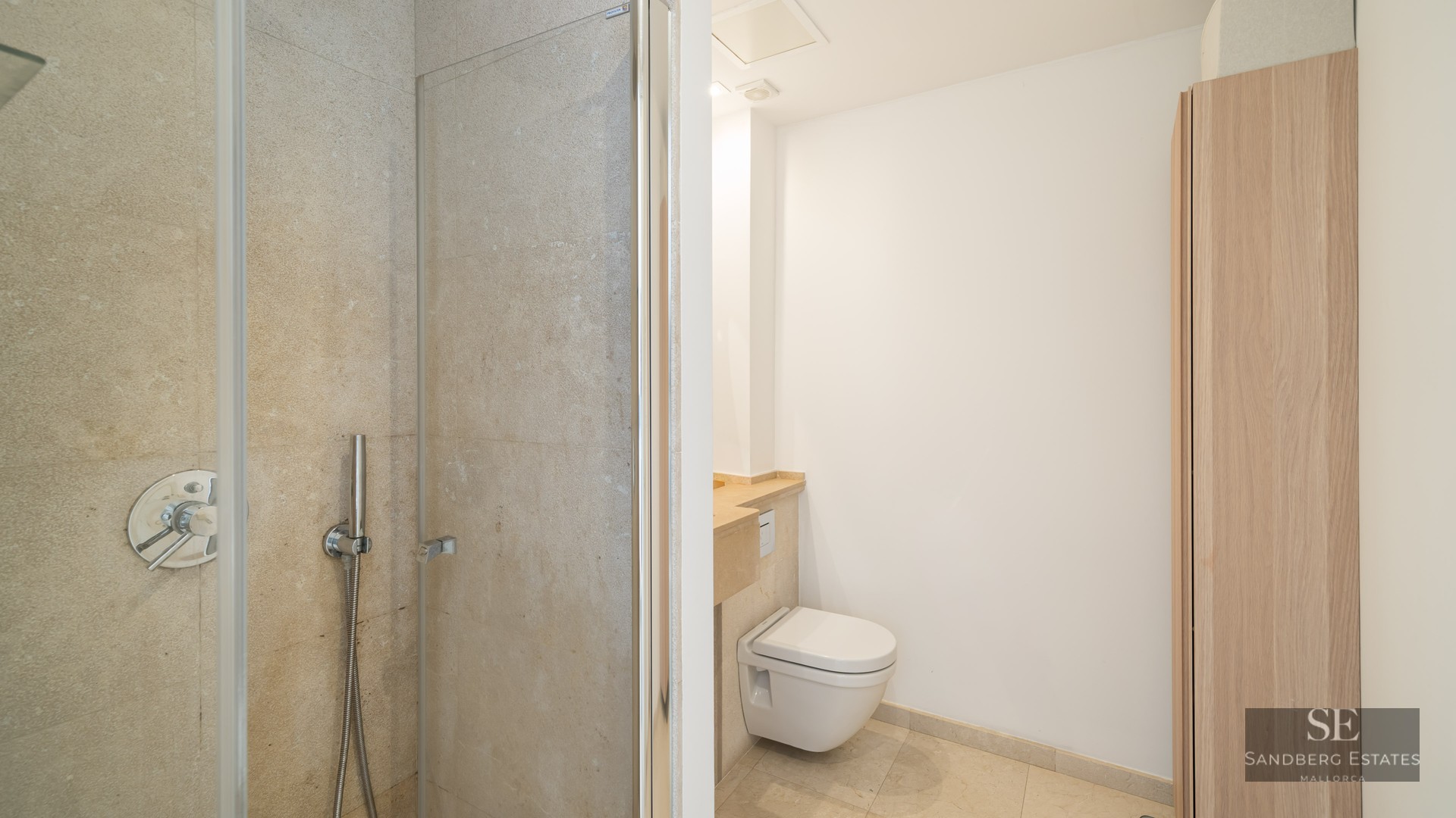 Bathroom featuring a glass walk-in shower, wall-mounted toilet, and beige stone walls.