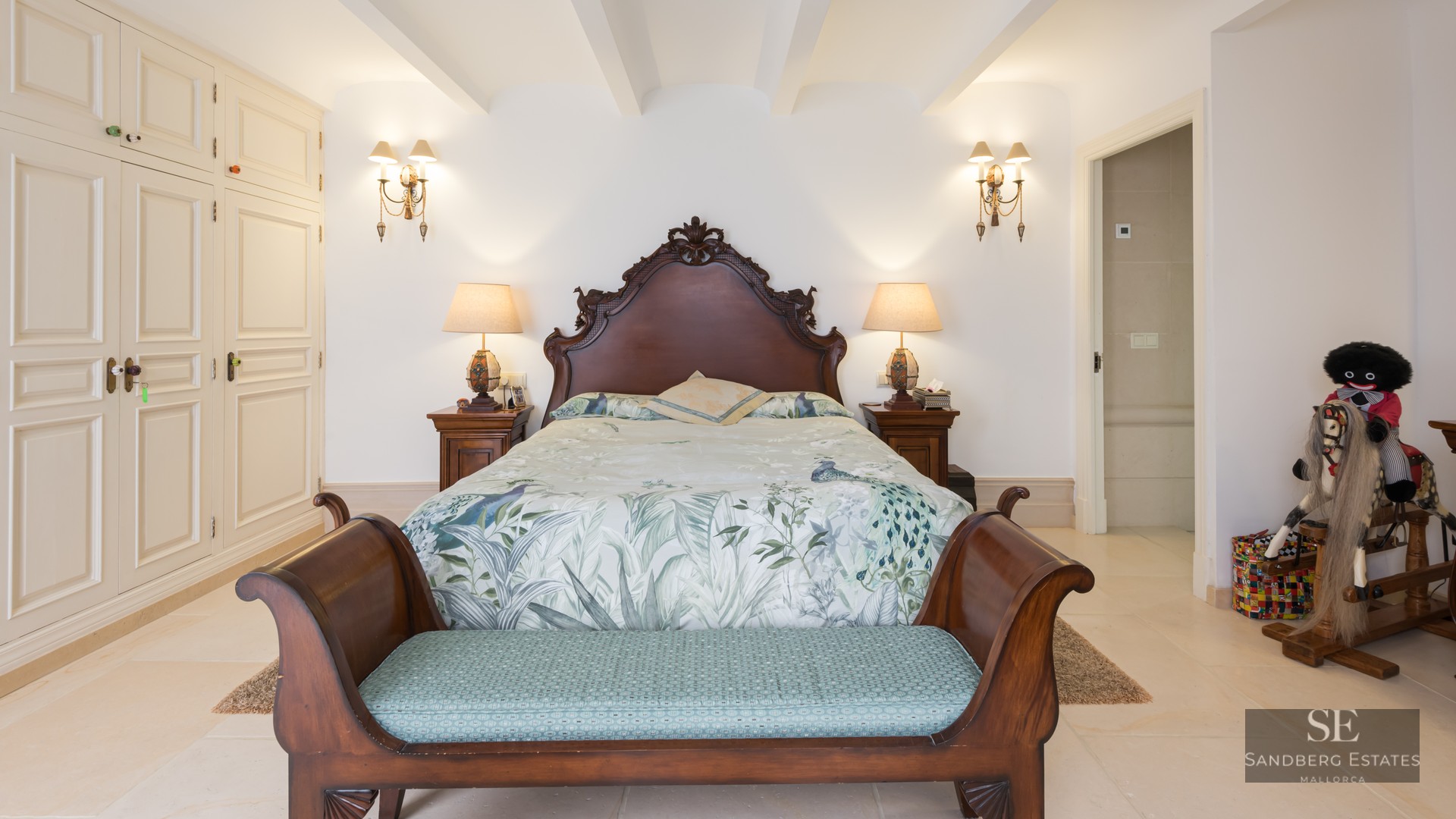 Bedroom featuring a large carved wood headboard, floral bedding, matching nightstands, and built-in white wardrobes.