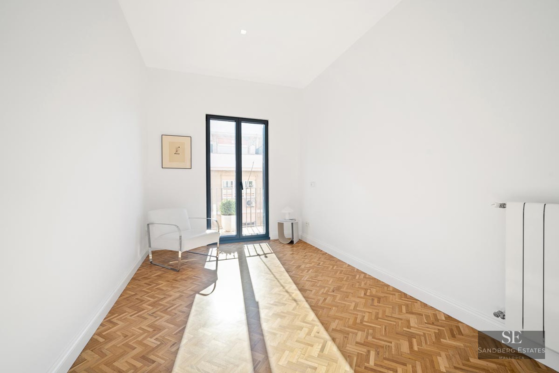 Bright white room featuring herringbone wood flooring, a white armchair, and a glass door to a balcony.