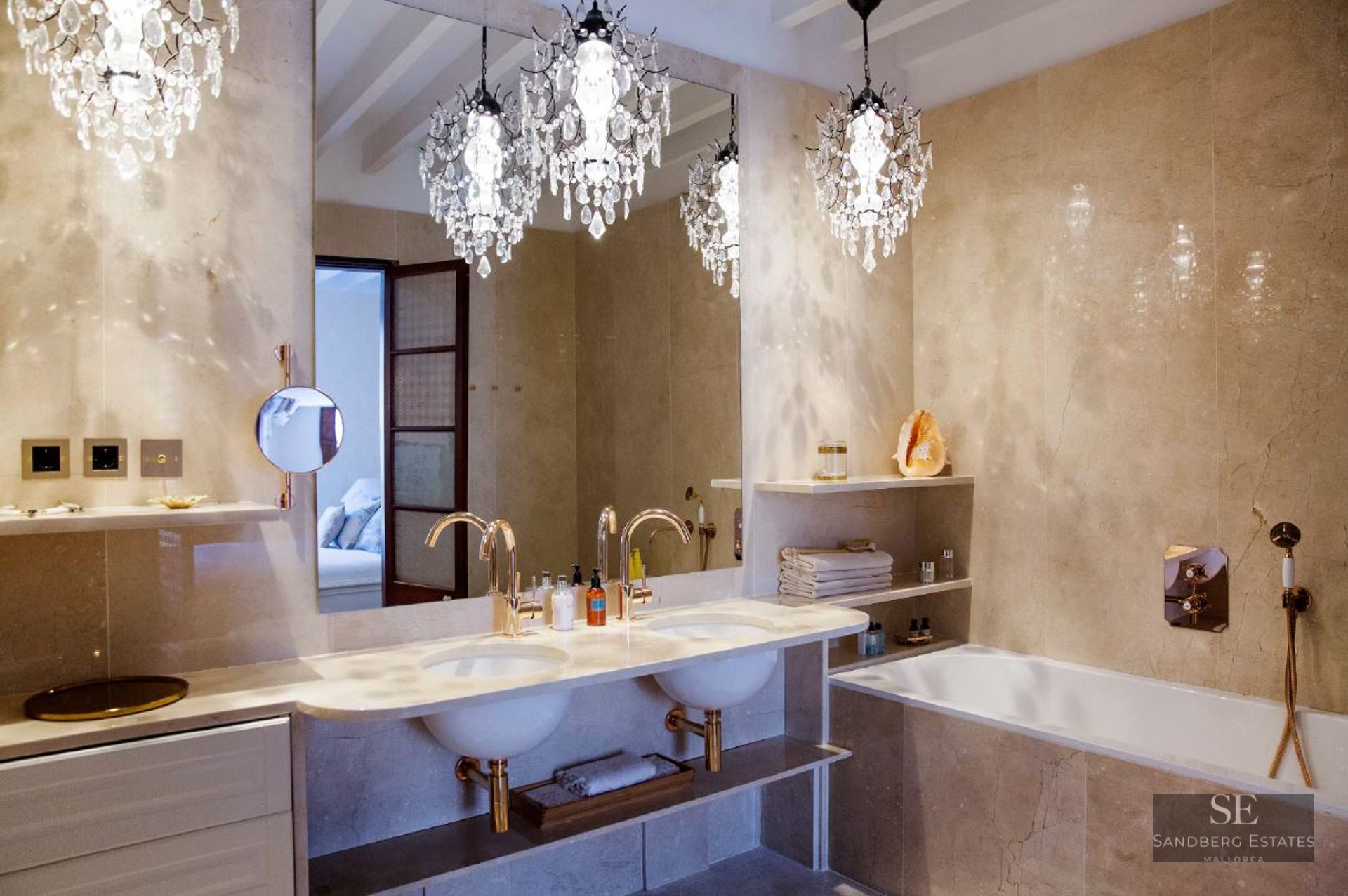 Luxurious bathroom featuring a double vanity, gold fixtures, marble walls, and three ornate crystal chandeliers.