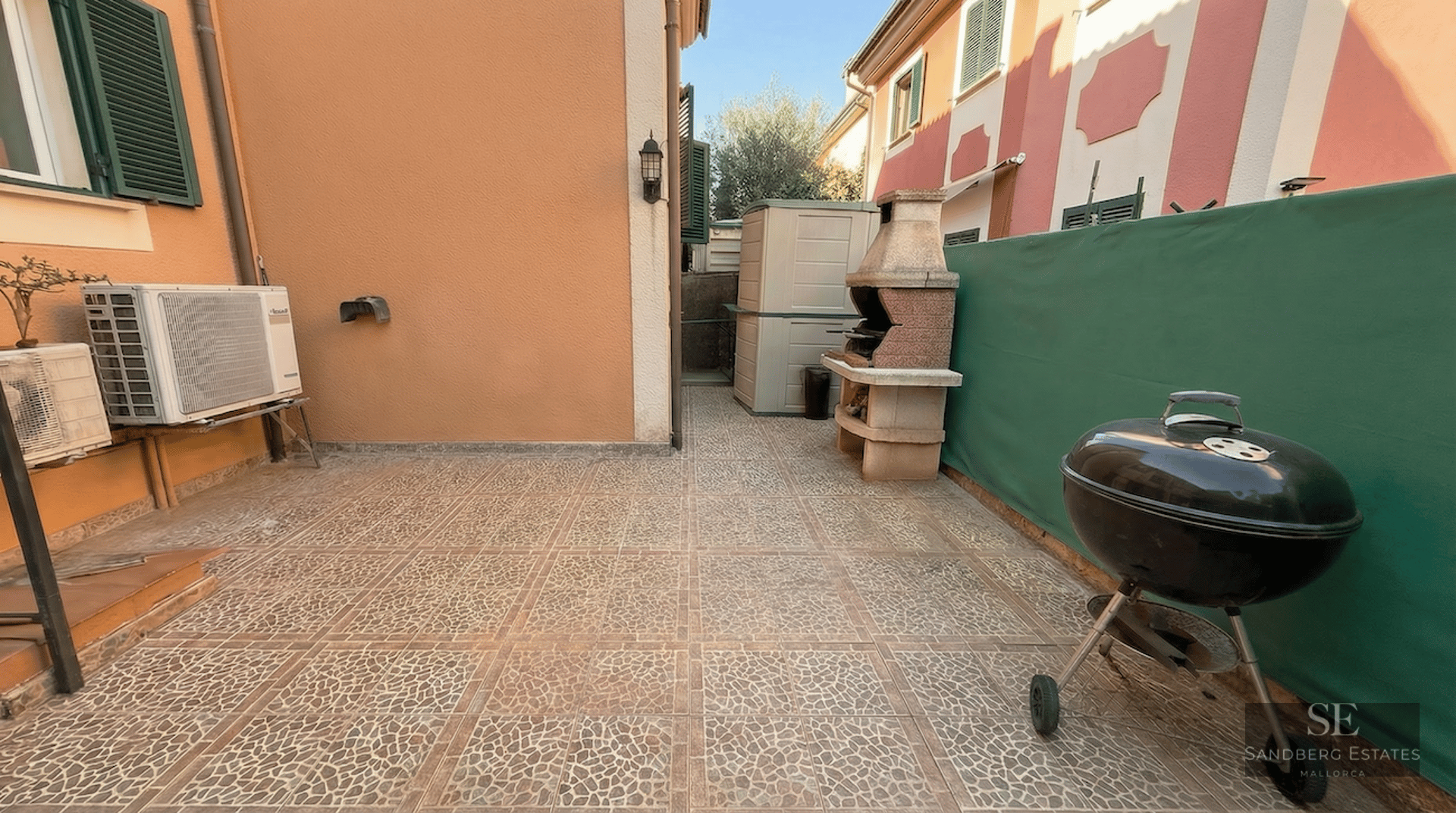 Outdoor patio with stone-patterned tiles, a masonry BBQ, a portable kettle grill, and a green privacy screen.