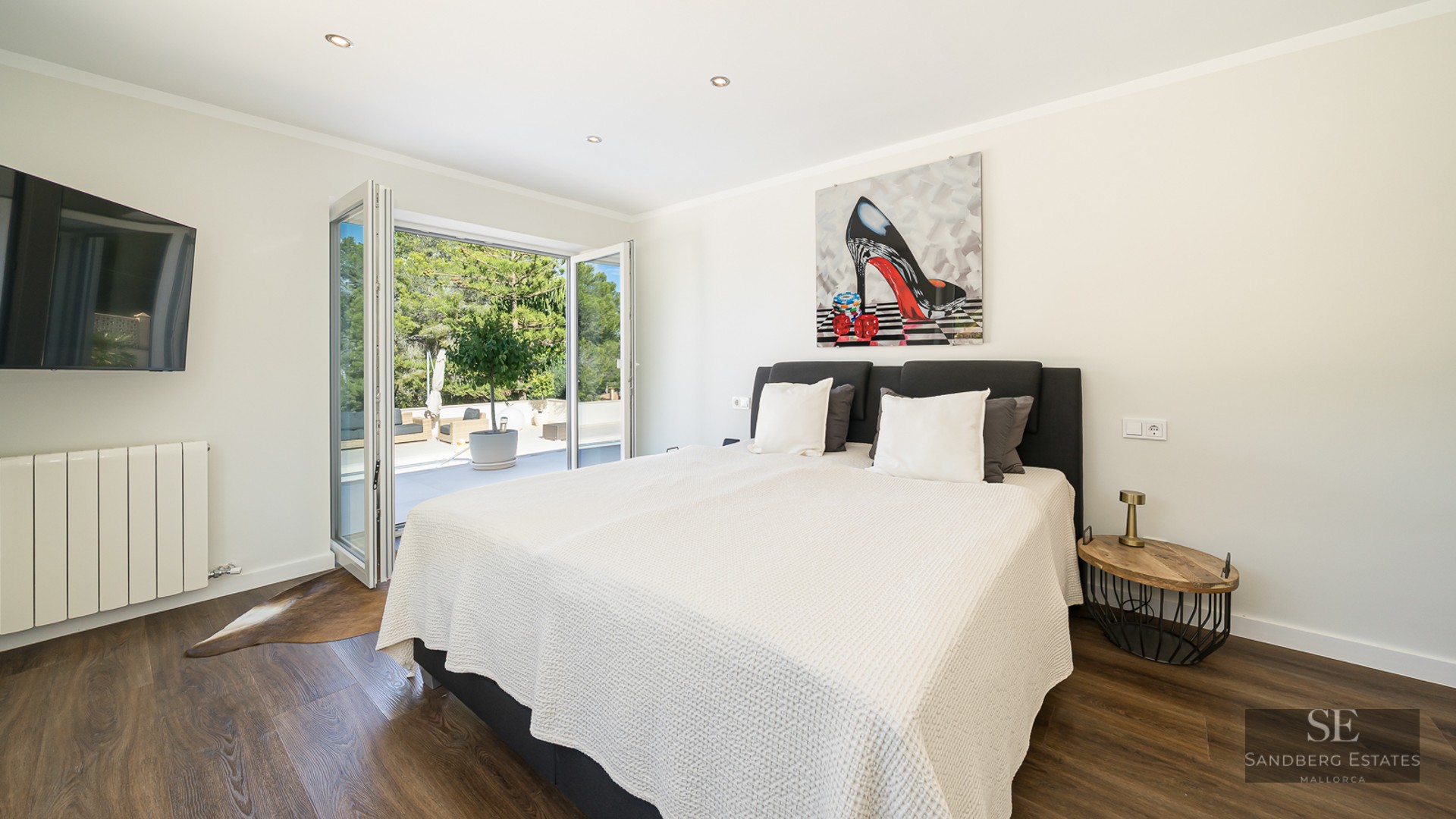 Chambre lumineuse avec grand lit, parquet foncé et portes vitrées pliantes ouvrant sur une terrasse ensoleillée.