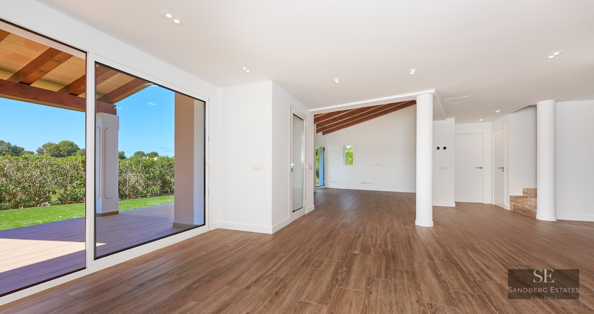 Large empty living room with wood floors, white walls, and sliding glass doors opening to a green garden.