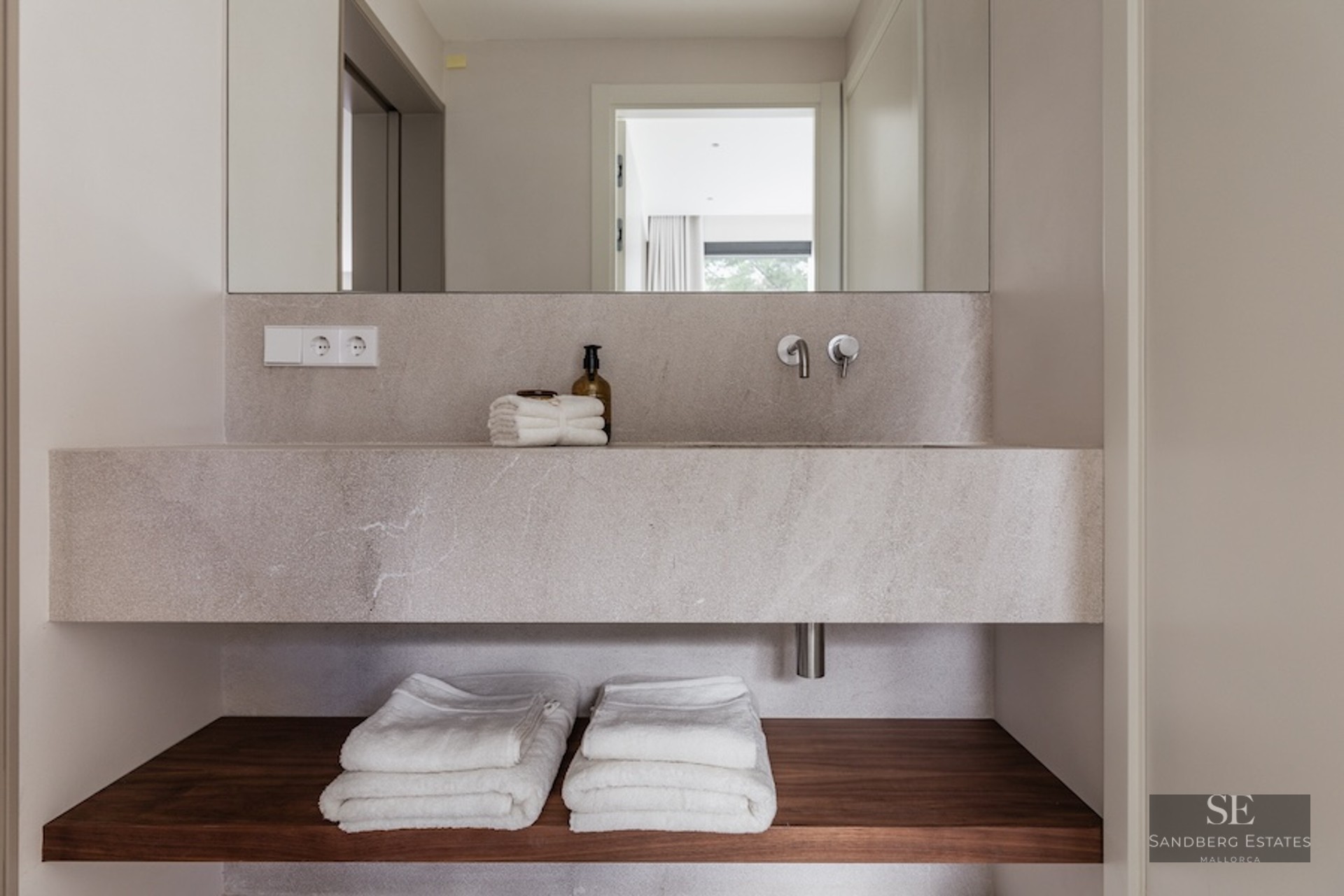 Close-up of a floating stone bathroom sink with a wooden shelf below and folded white towels.