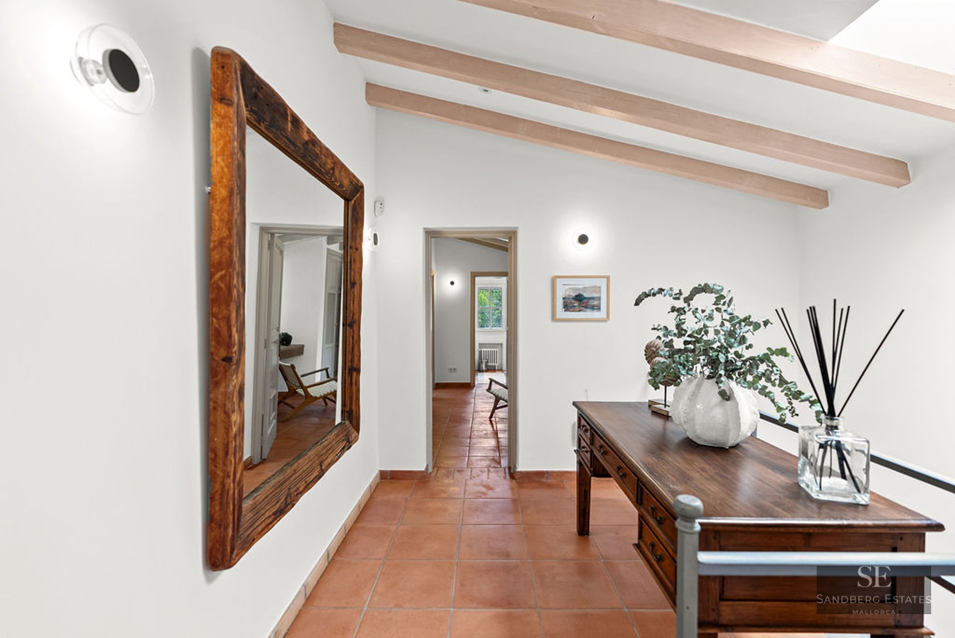 Hallway with orange tile floor, large wooden mirror, antique desk, and exposed ceiling beams.