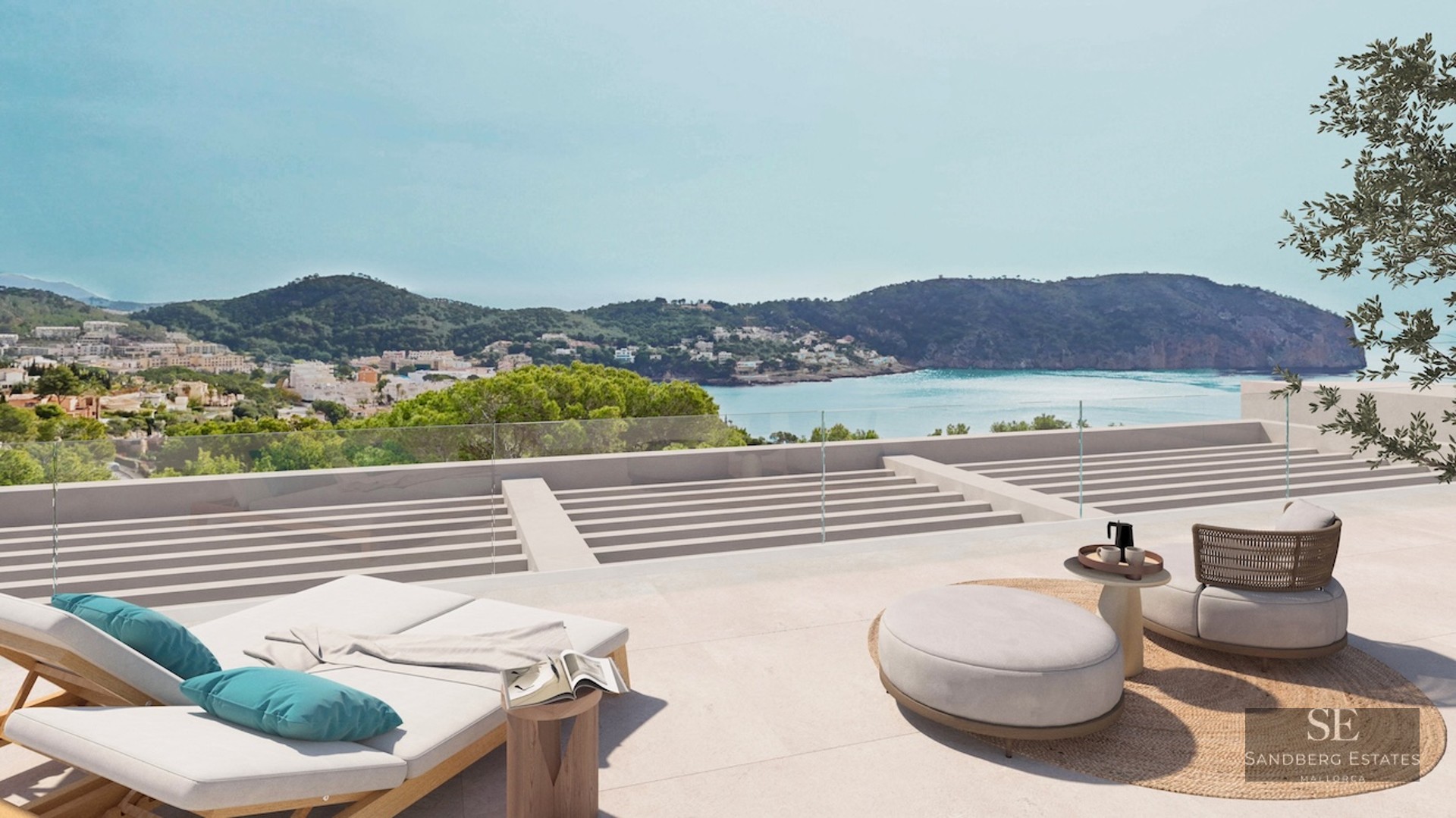 Modern terrace with sun loungers and outdoor seating overlooking a turquoise bay and lush green mountains.
