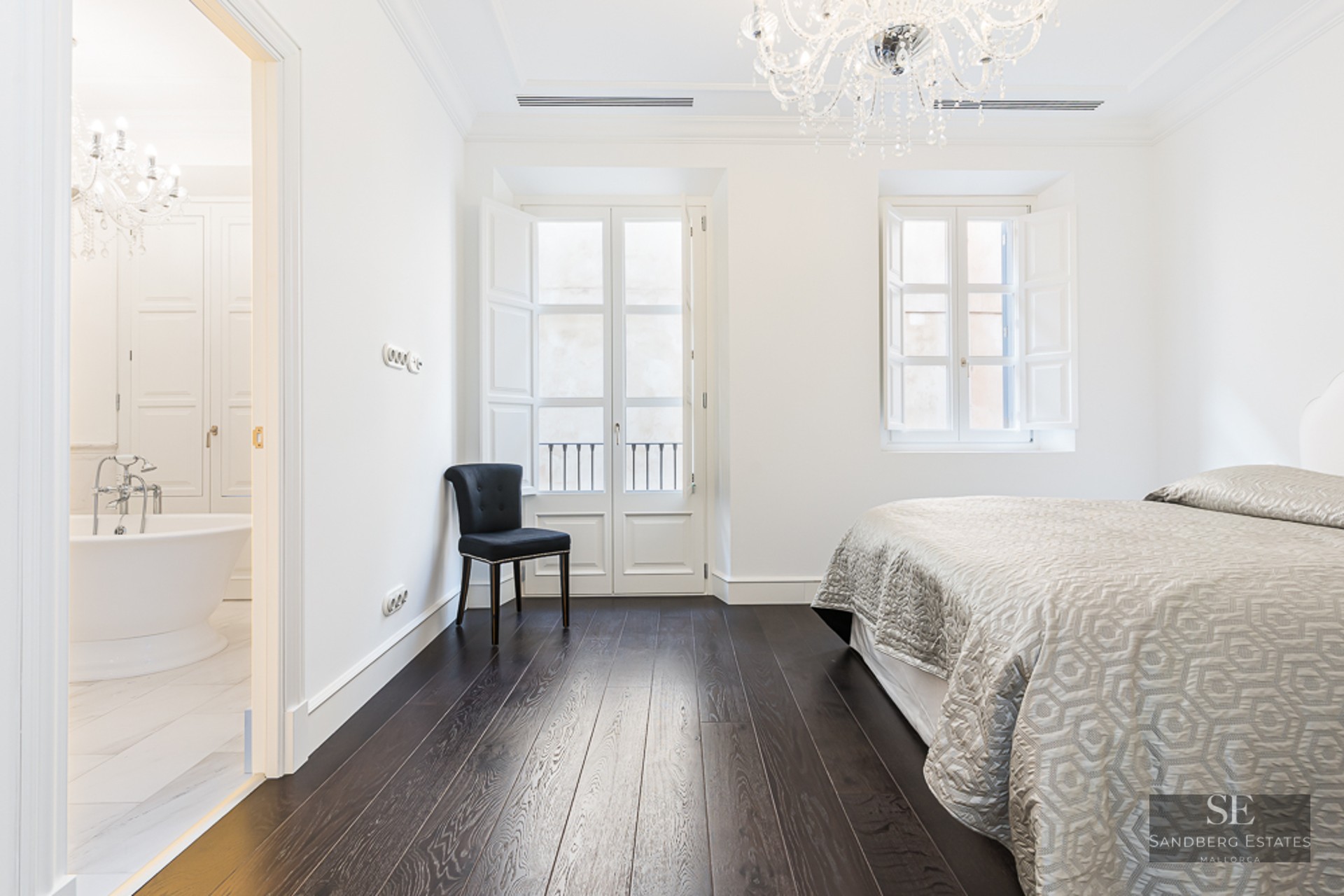 Master bedroom featuring dark wood floors, crystal chandelier, and a view into a marble bathroom with a bathtub.