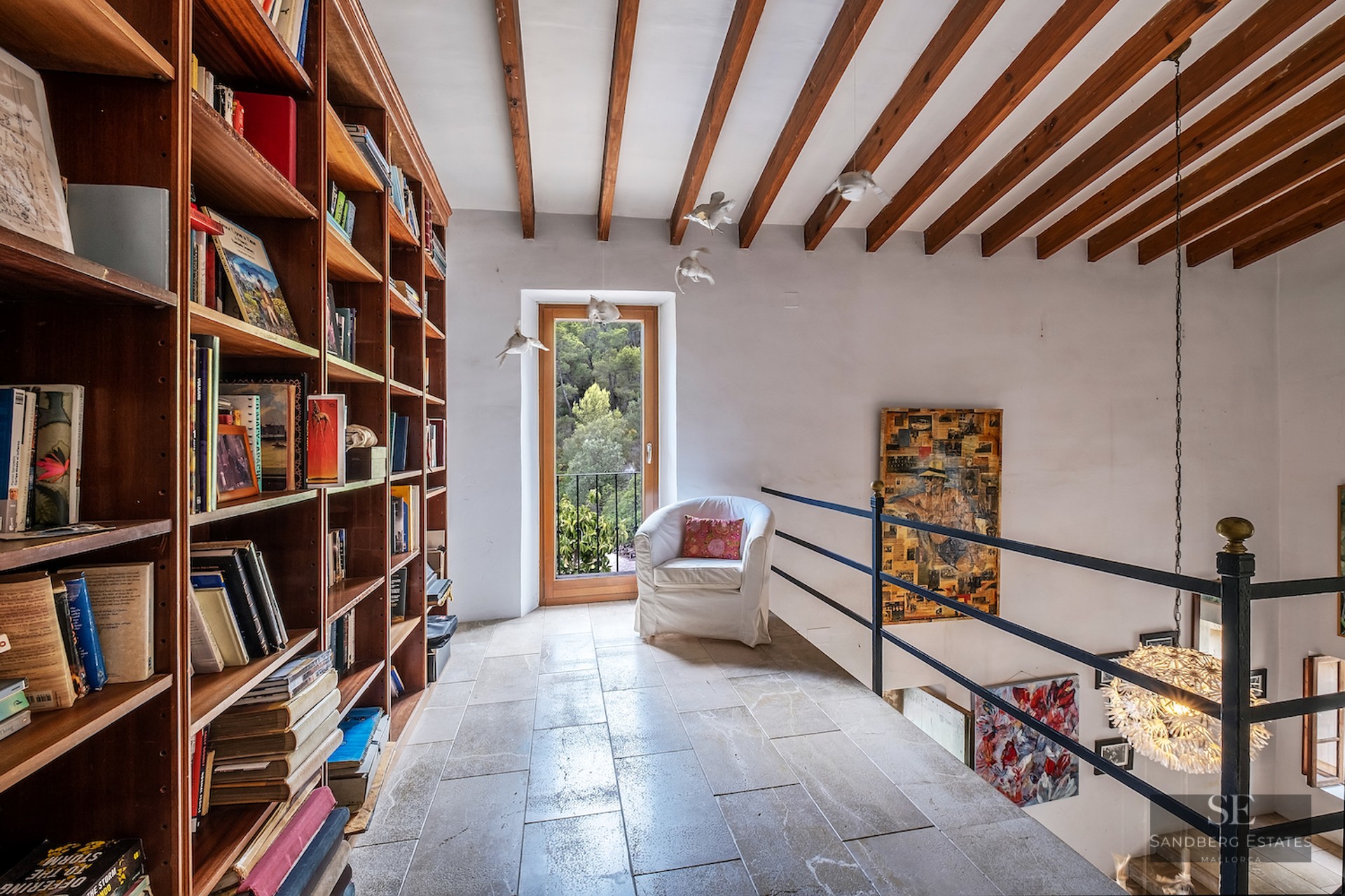 Mezzanine library featuring floor-to-ceiling wooden bookshelves, stone flooring, and rustic exposed ceiling beams.