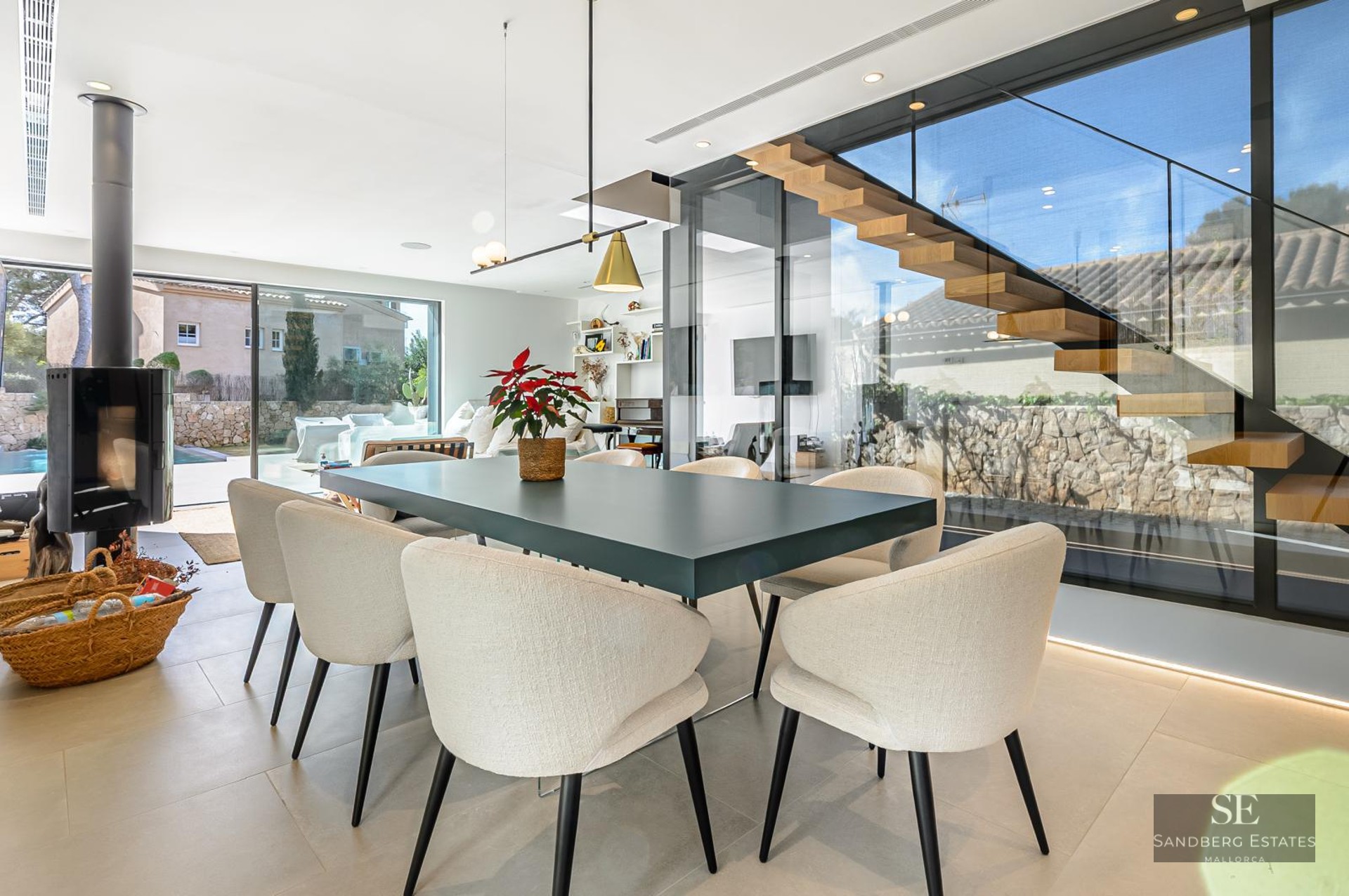 Contemporary dining room featuring a dark table, beige chairs, a floating wooden staircase, and large glass windows.
