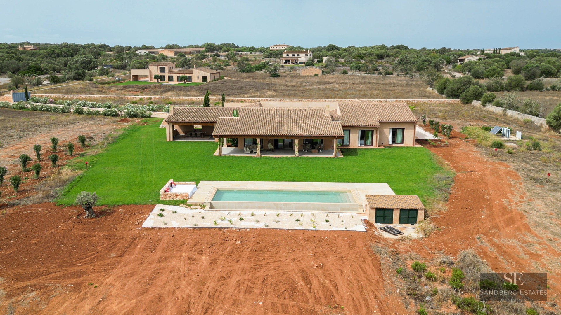 Bird's eye view of a luxury villa with terracotta roof, rectangular swimming pool, and large green lawn.