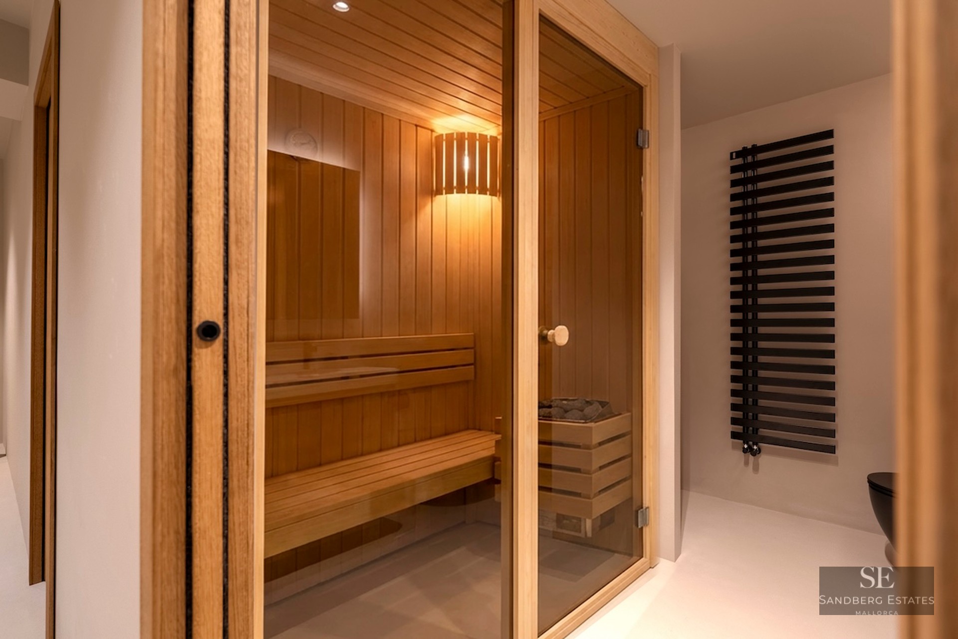 Sauna en bois clair avec porte vitrée, bancs à plusieurs niveaux et éclairage intérieur chaleureux.