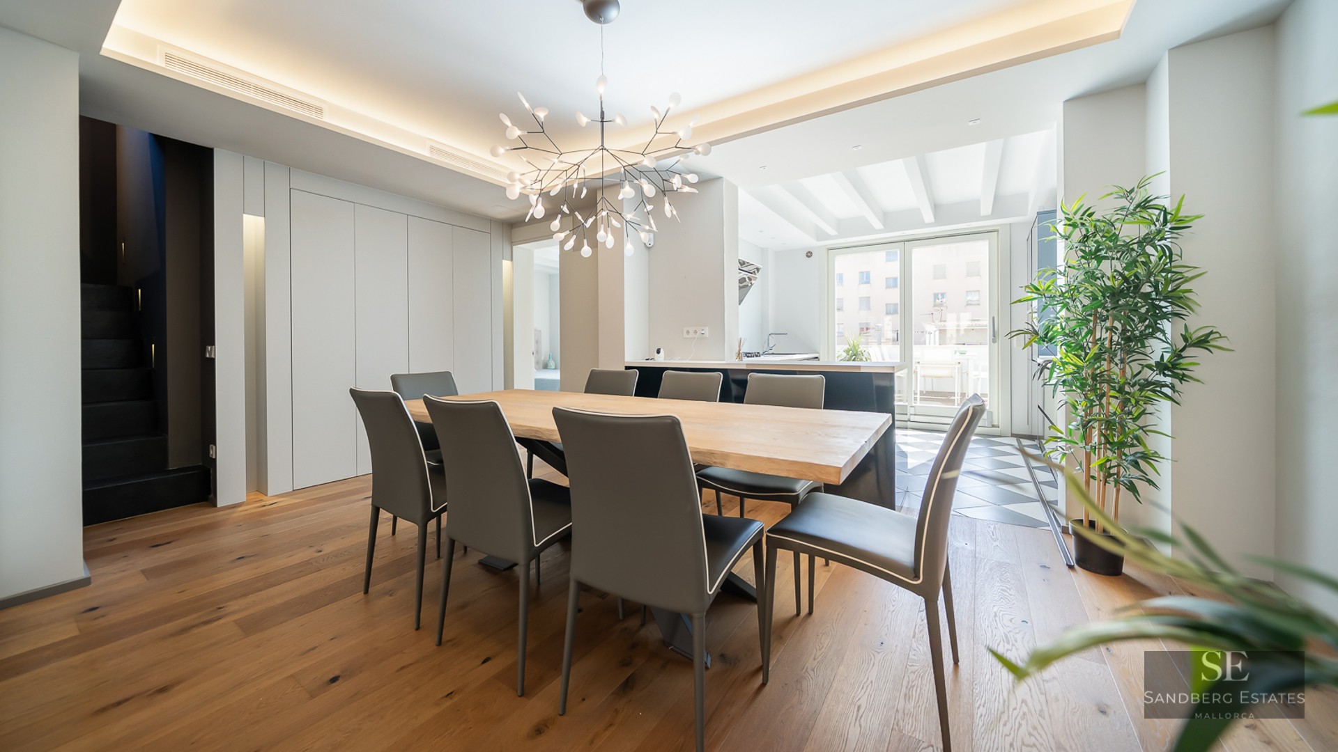 Modern dining room with a large light wood table, eight charcoal chairs, and a branch-style chandelier.